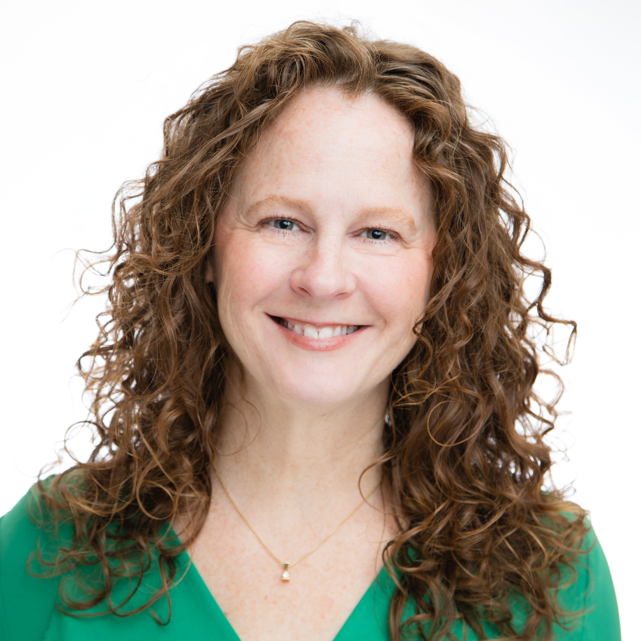 Headshot of a woman with red-curly hair and green eyes, wearing a green shirt on a white background. Photographed in studio by Amanda Faucett Photography.