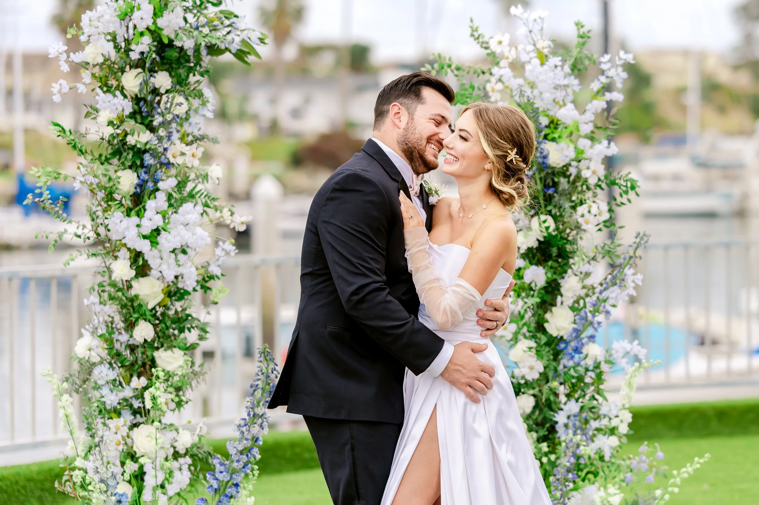 Bride and groom embracing outdoors with floral arch backdrop.