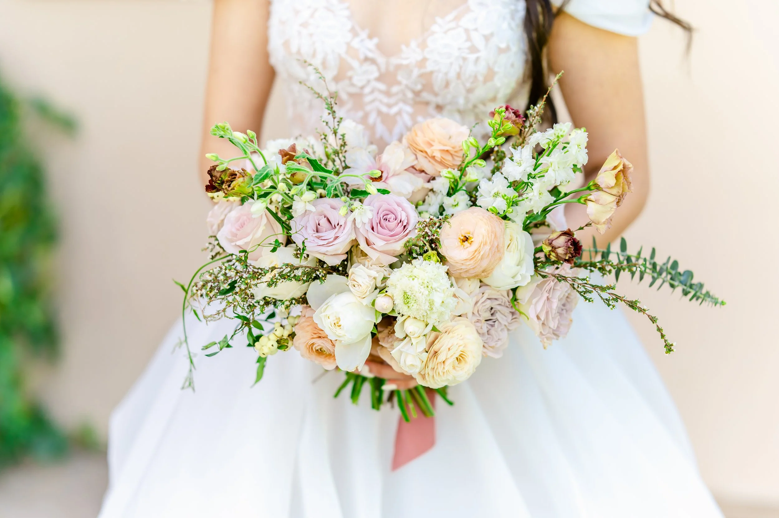 Bride holding a bouquet of pastel flowers, including roses and peonies, with greenery.