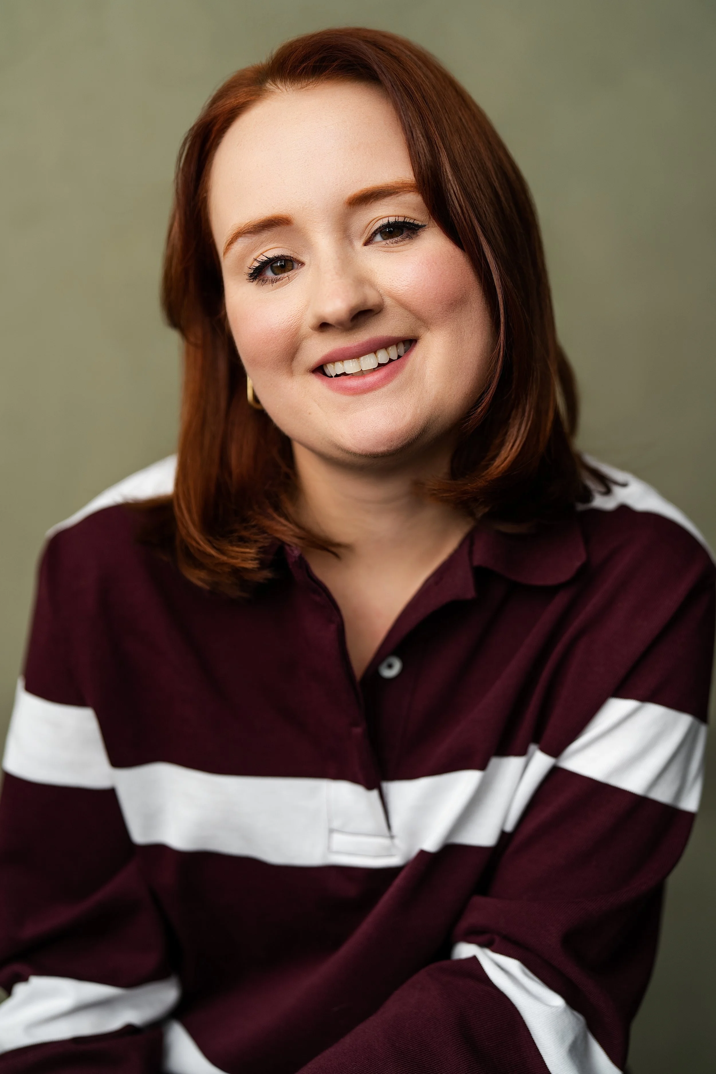 A women with shoulder length red hair in a striped maroon rugby shirt