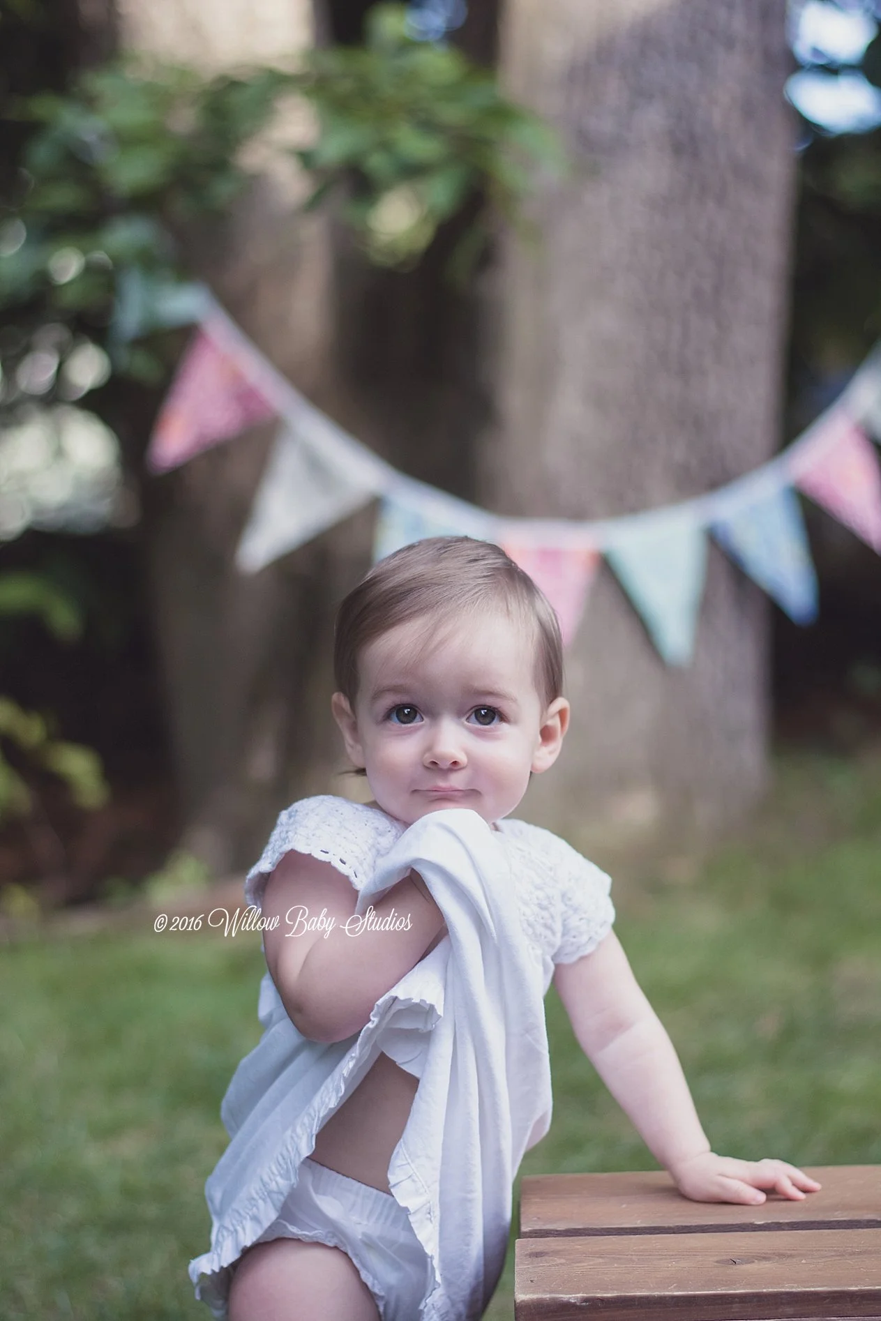 one year old staring at camera holding her dress up to her chin