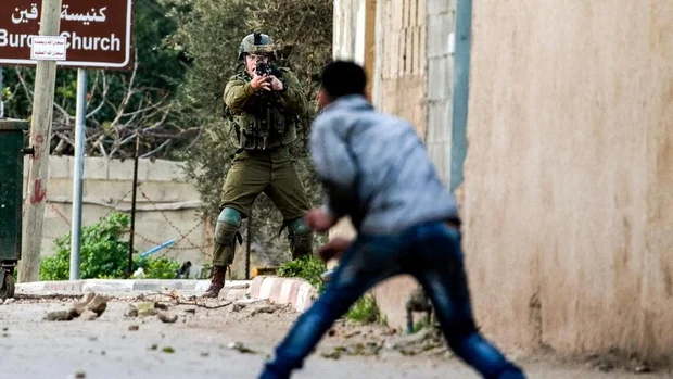 An Israeli soldier points his weapons at a youth during clashes in Burqin in February 2018 (AFP)