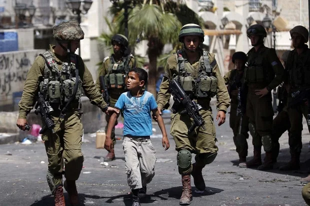 Israeli soldiers arrest a young Palestinian boy following clashes in Hebron in June 2014 (AFP)