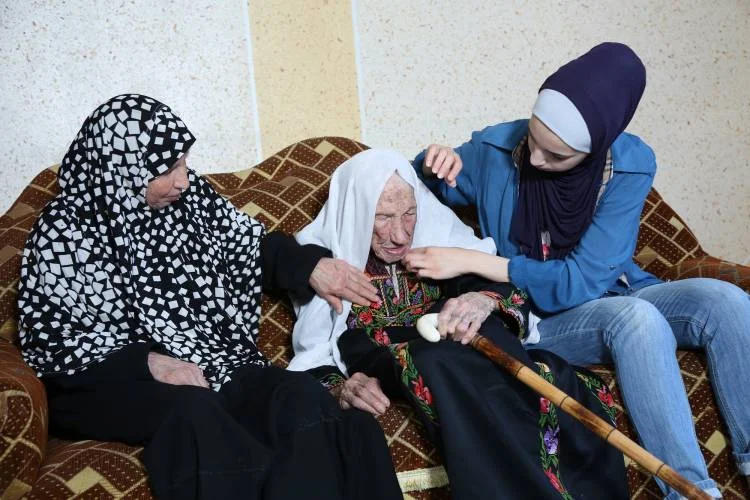 65-year-old Zainab Atallah, Hakma’s daughter (left), 105-year-old Hakma Atallah (middle) and 19-year-old Haneen Atallah, Hakma’s granddaughter (right) © 2018 UNRWA Photo by Mohammed Hinnawi.