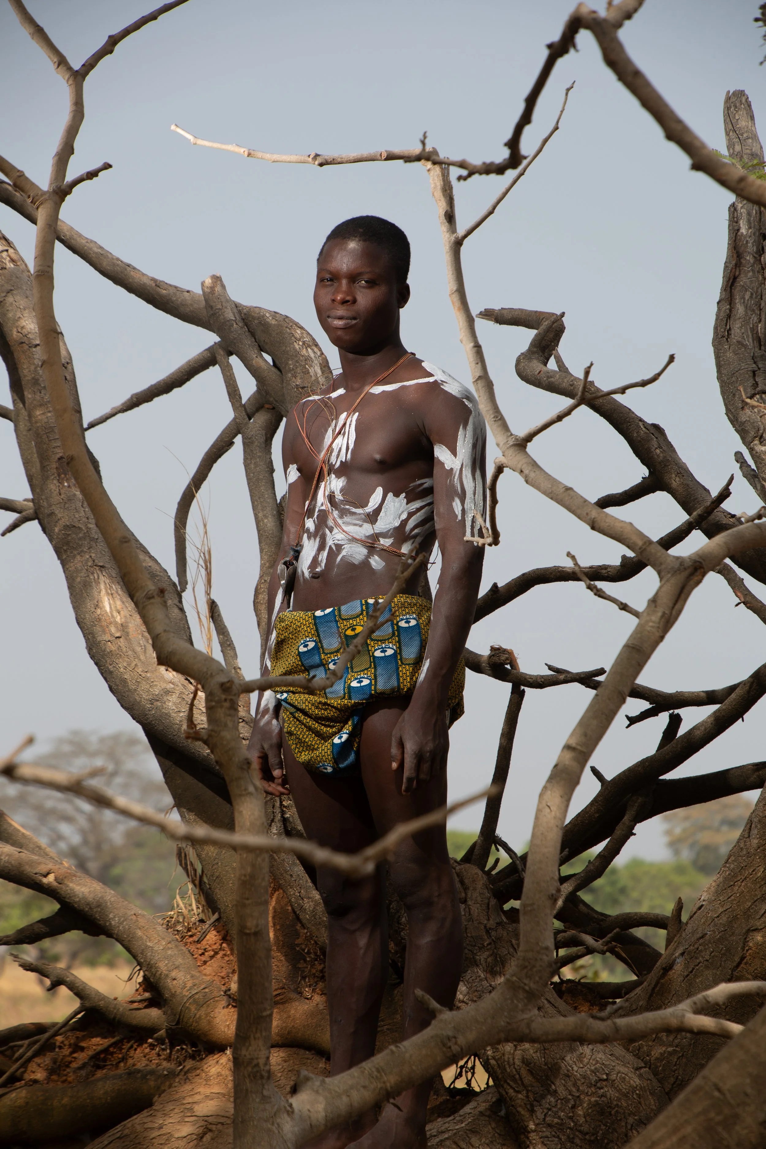 Barefoot on roots, his frame upright against a tree older than memory.