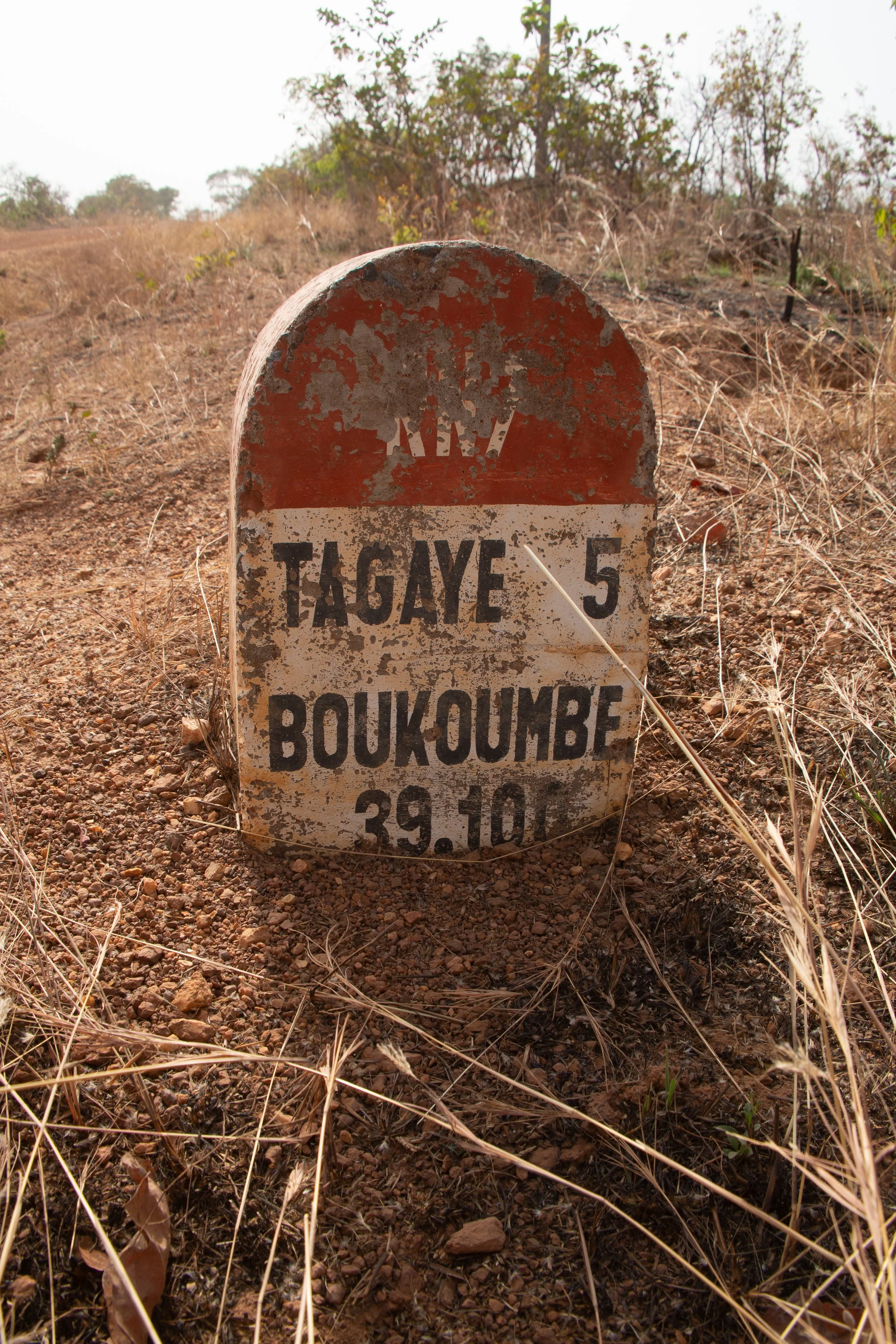 A milestone marks the road: Tagaye 5 / Boukoumbé 39. Time measured in dust and stone.