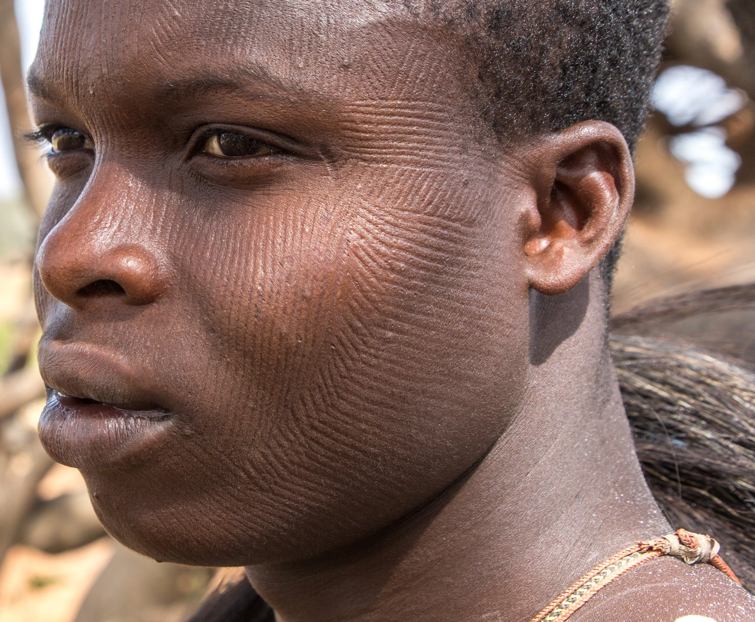 Scarification across his face. Marks of identity. Marks of memory.