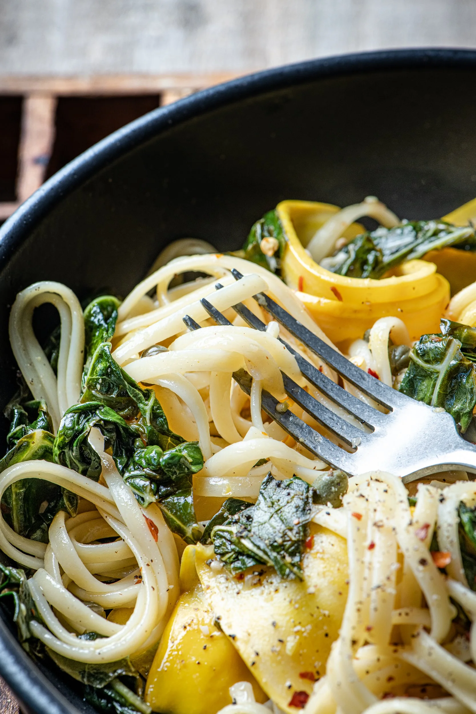 Close of up a bowl of linguini pasta with ribbons of zucchini, sauted kale and capers