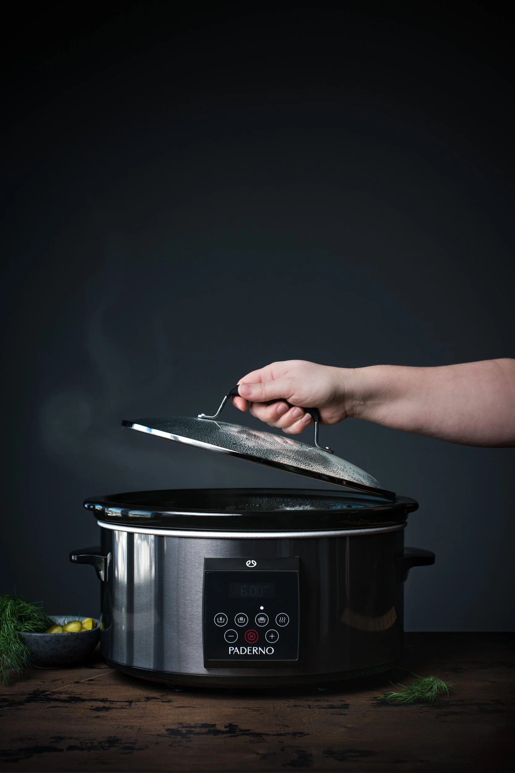Woman's hand slowly opening the lid of slow cooker with steam escaping
