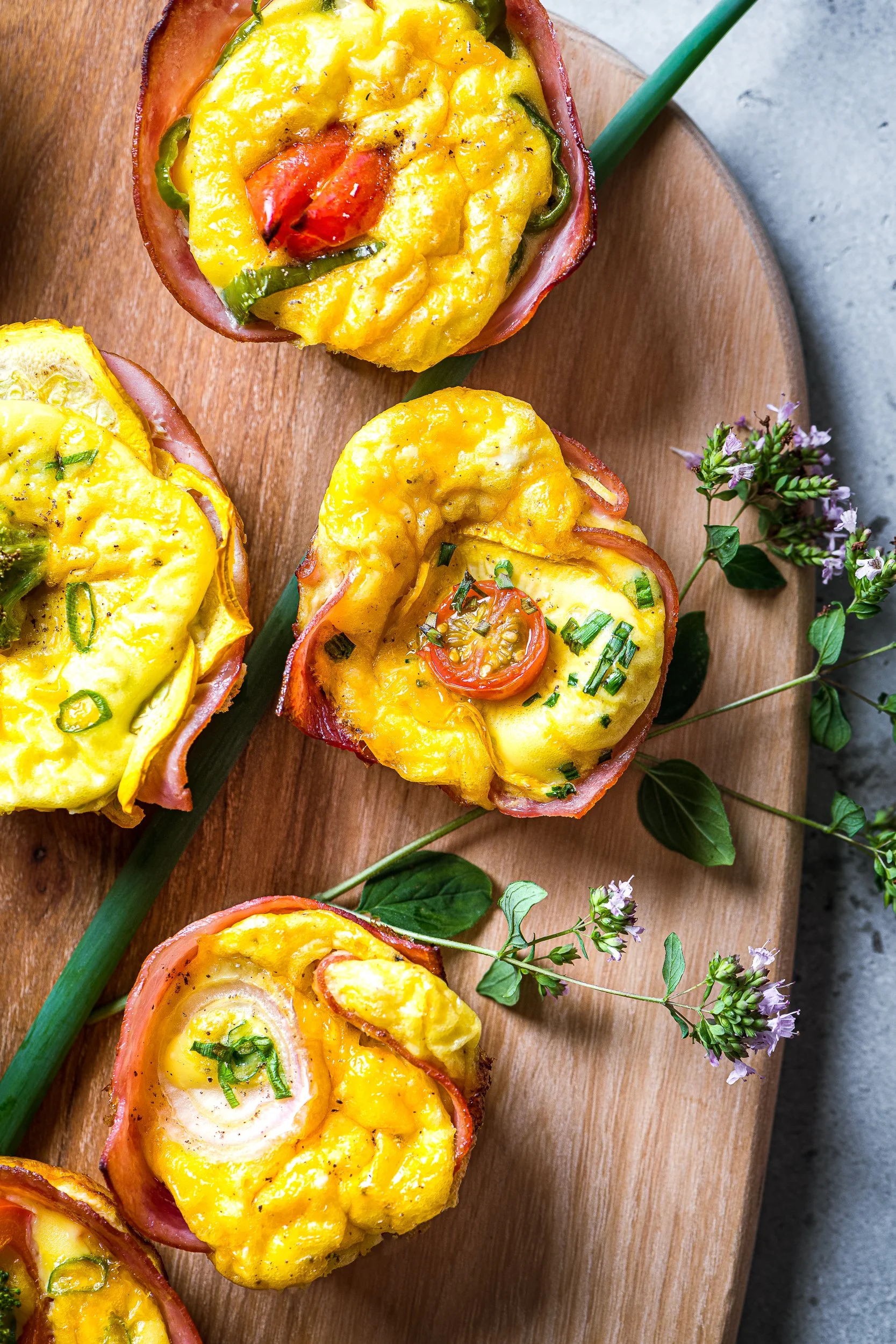 Four cooked eggs cups in ham on a cutting board with some flowering oregano