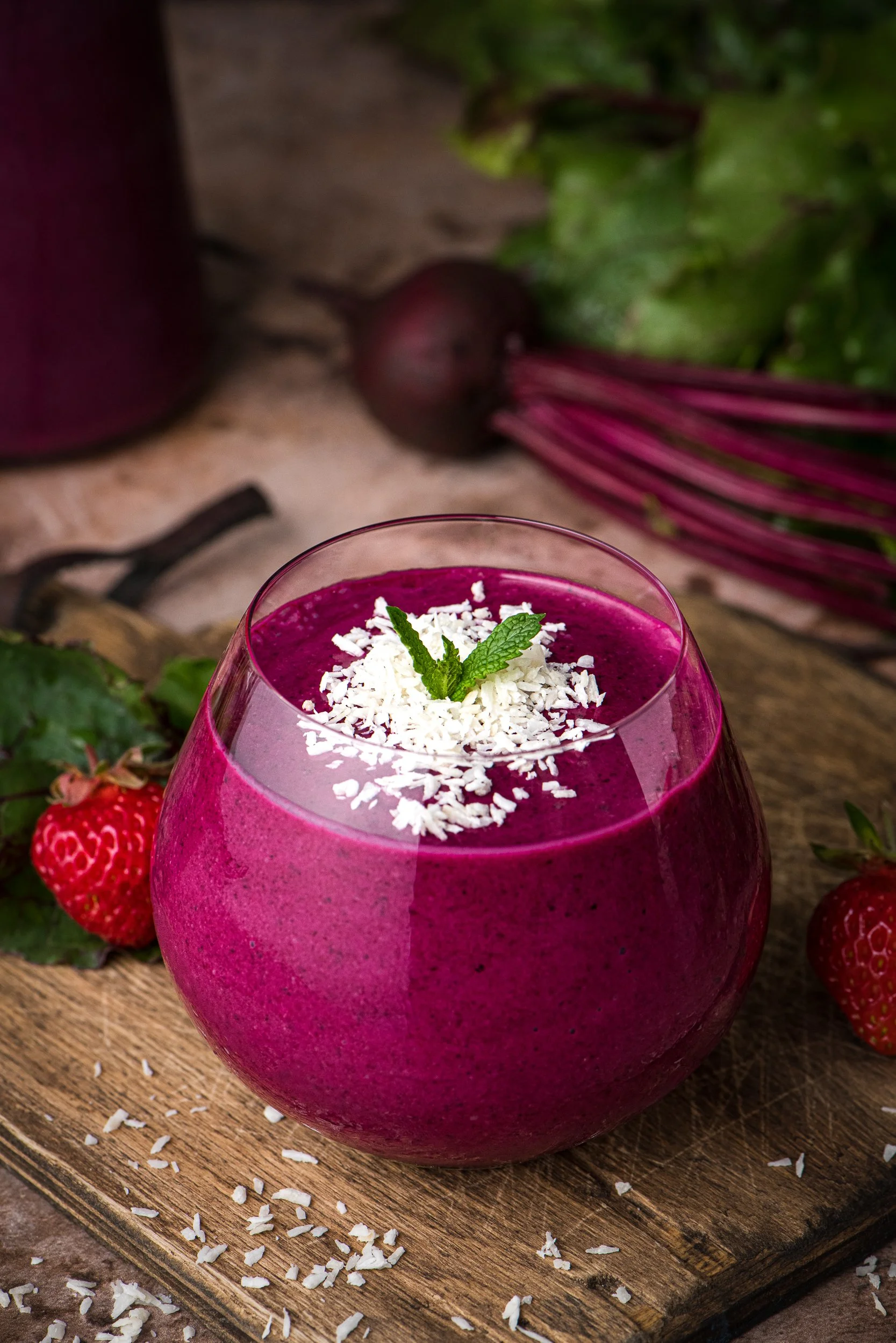 Glass on a cutting board filled with a beet and berry smoothie, sprinkled with coconut