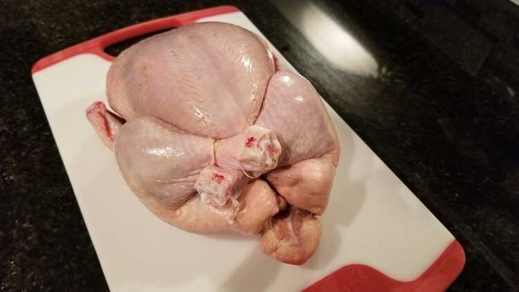 Using kitchen knife to cut raw chicken leg away from flesh