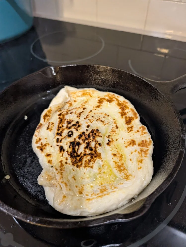 garlic naan cooking in a cast iron skillet