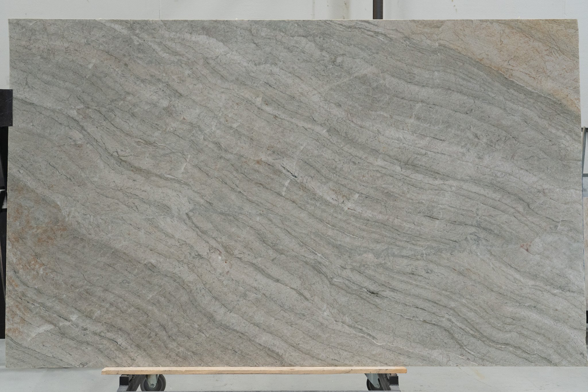 En stor plade af beige og grå marmoreffekt med naturlige striber og kornmønster, placeret på en vogn med hjul i en industriel setting.