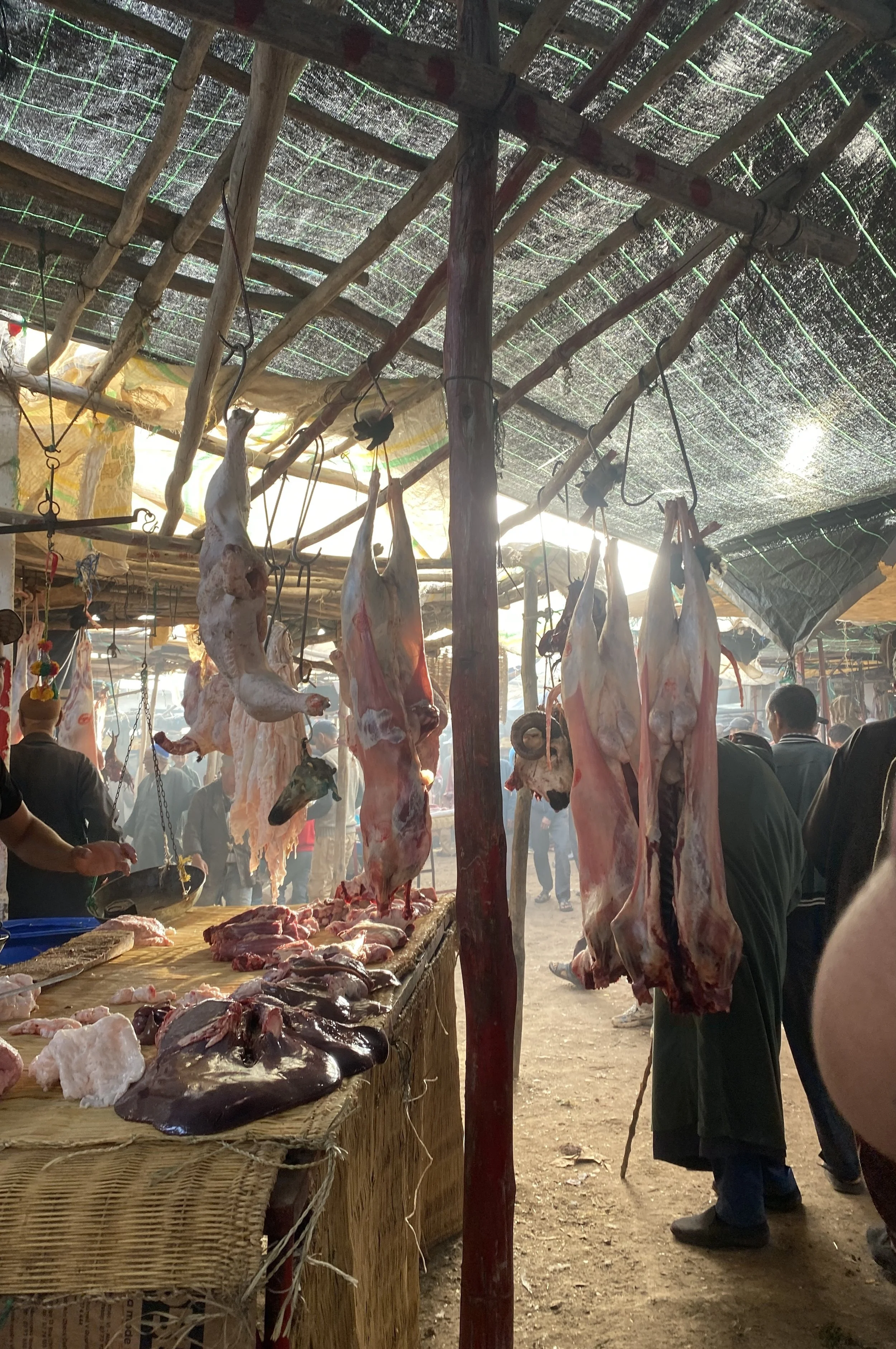 Butchered animals hang from their feet in a market. Other cuts sit on a table