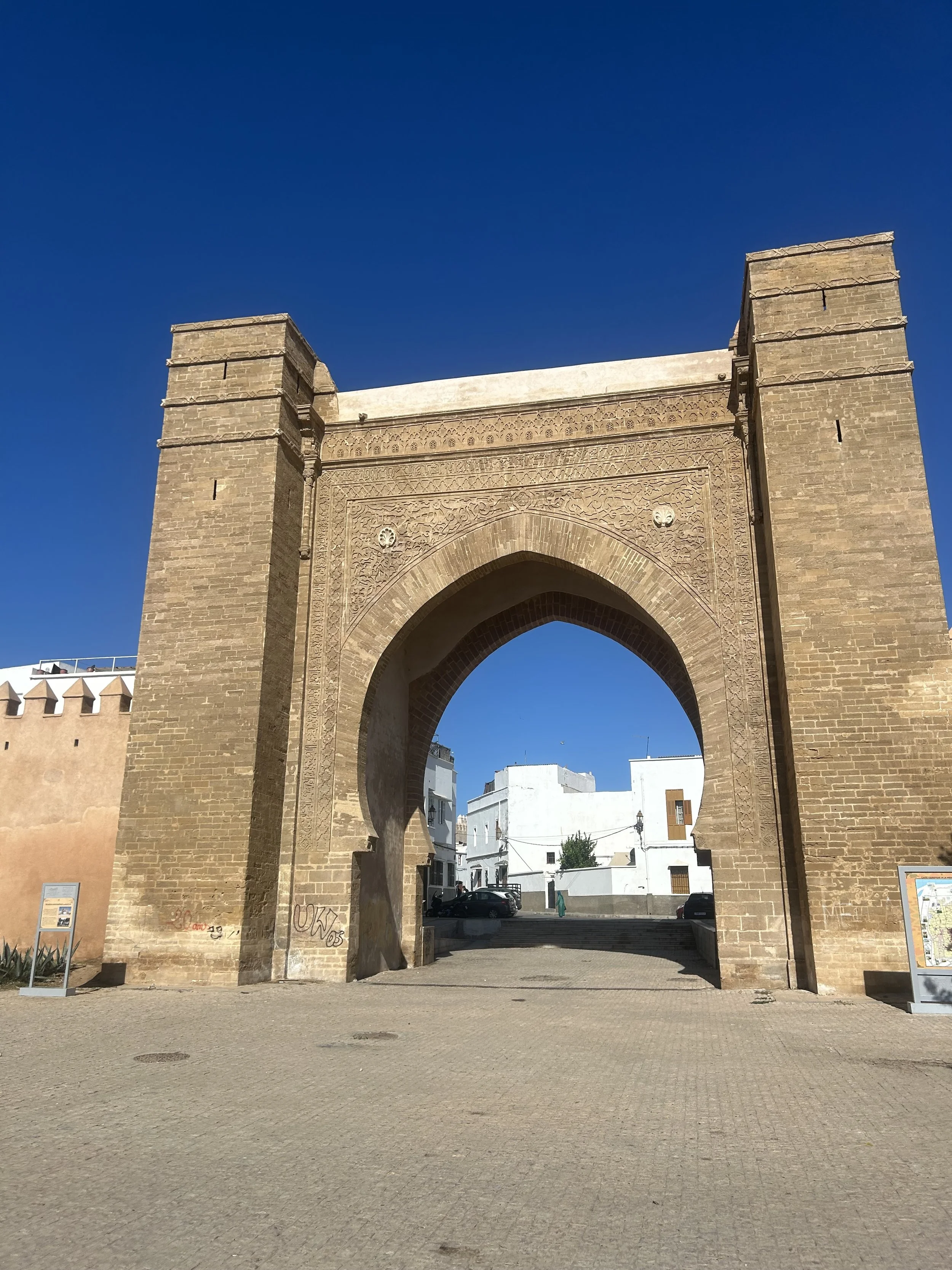 A large stone arched gateway is part of a tan wall. Inside, white homes are visible.