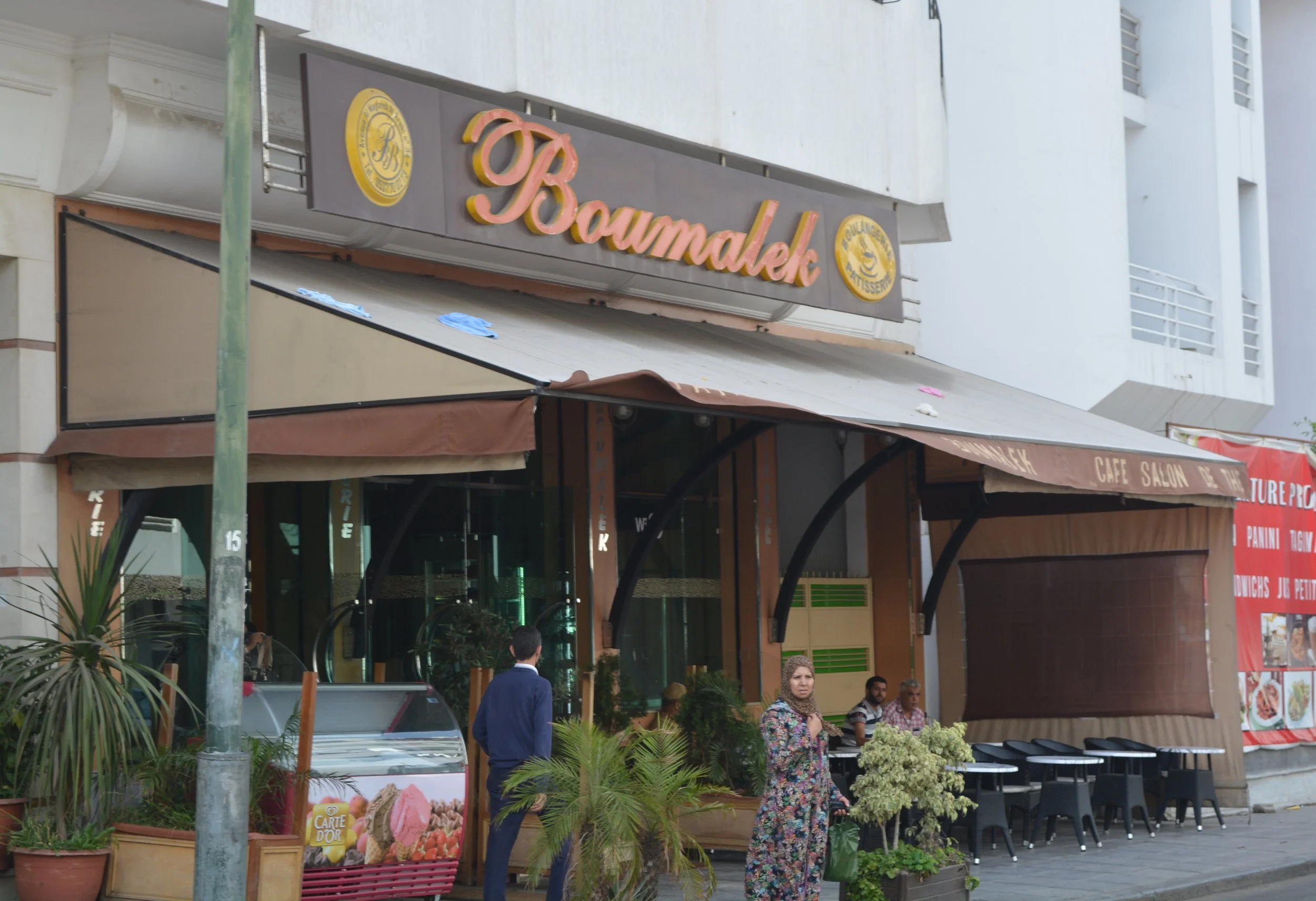 The outside of Boumalek cafe with an awning and space for seating and an ice cream cooler