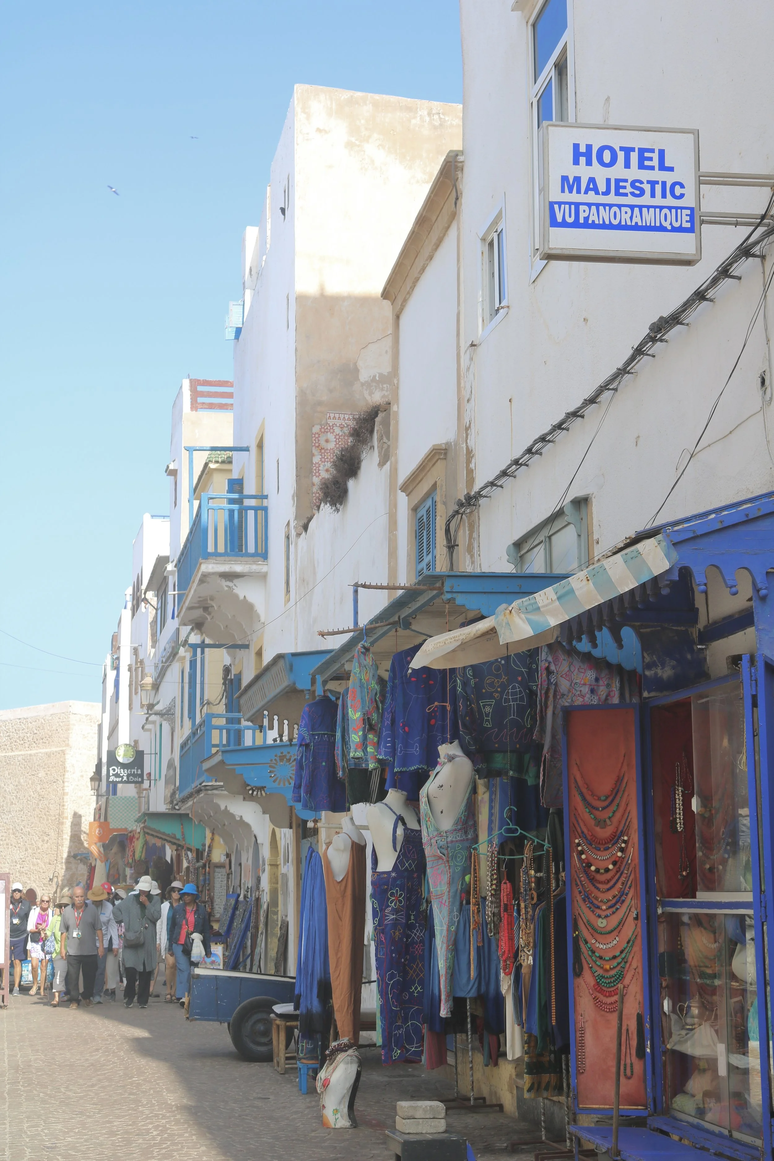 In the city, shops line a street with white buildings and blue trim