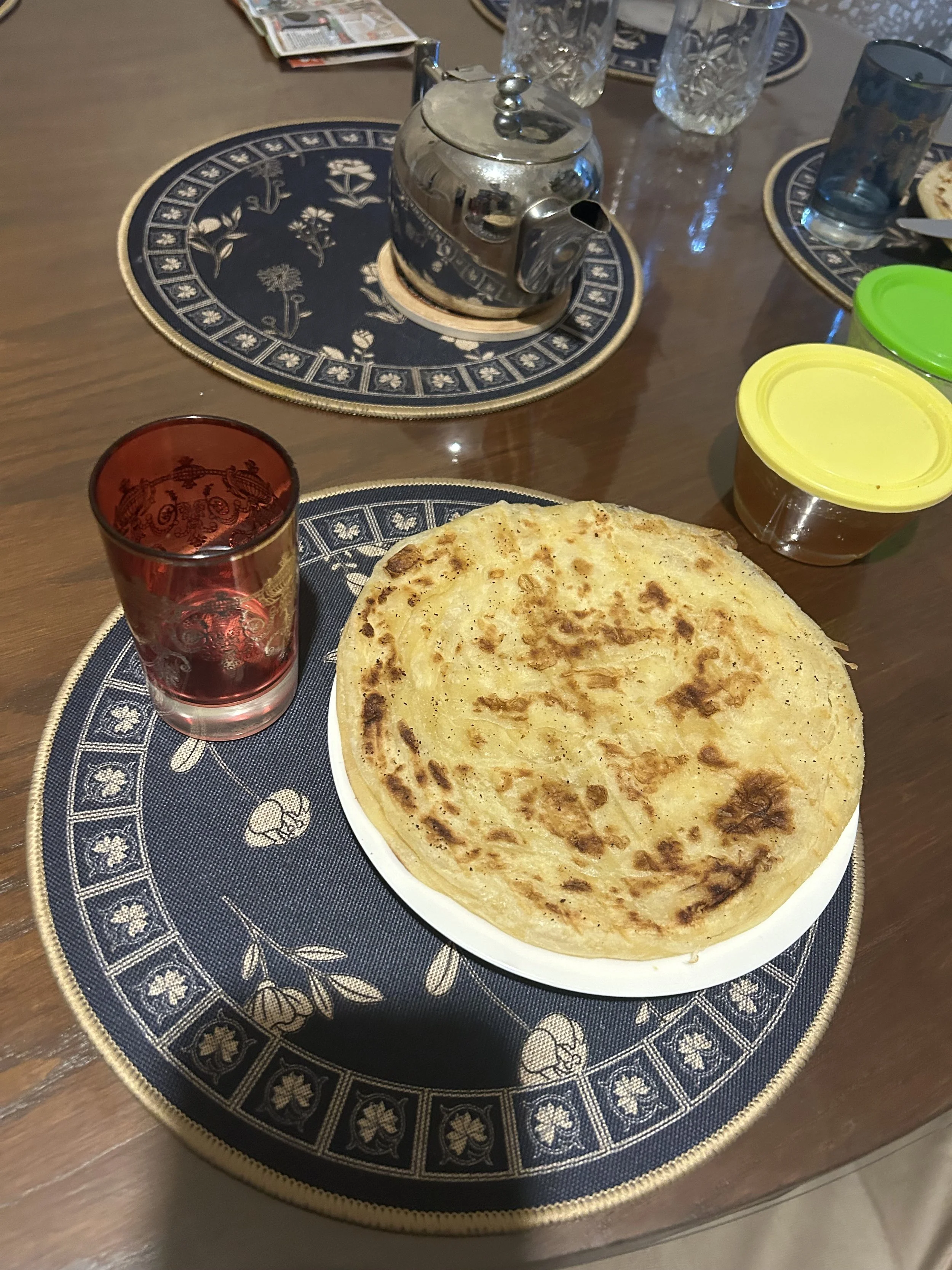 A plate with msimmin sits on a table with a glass and a pot of tea