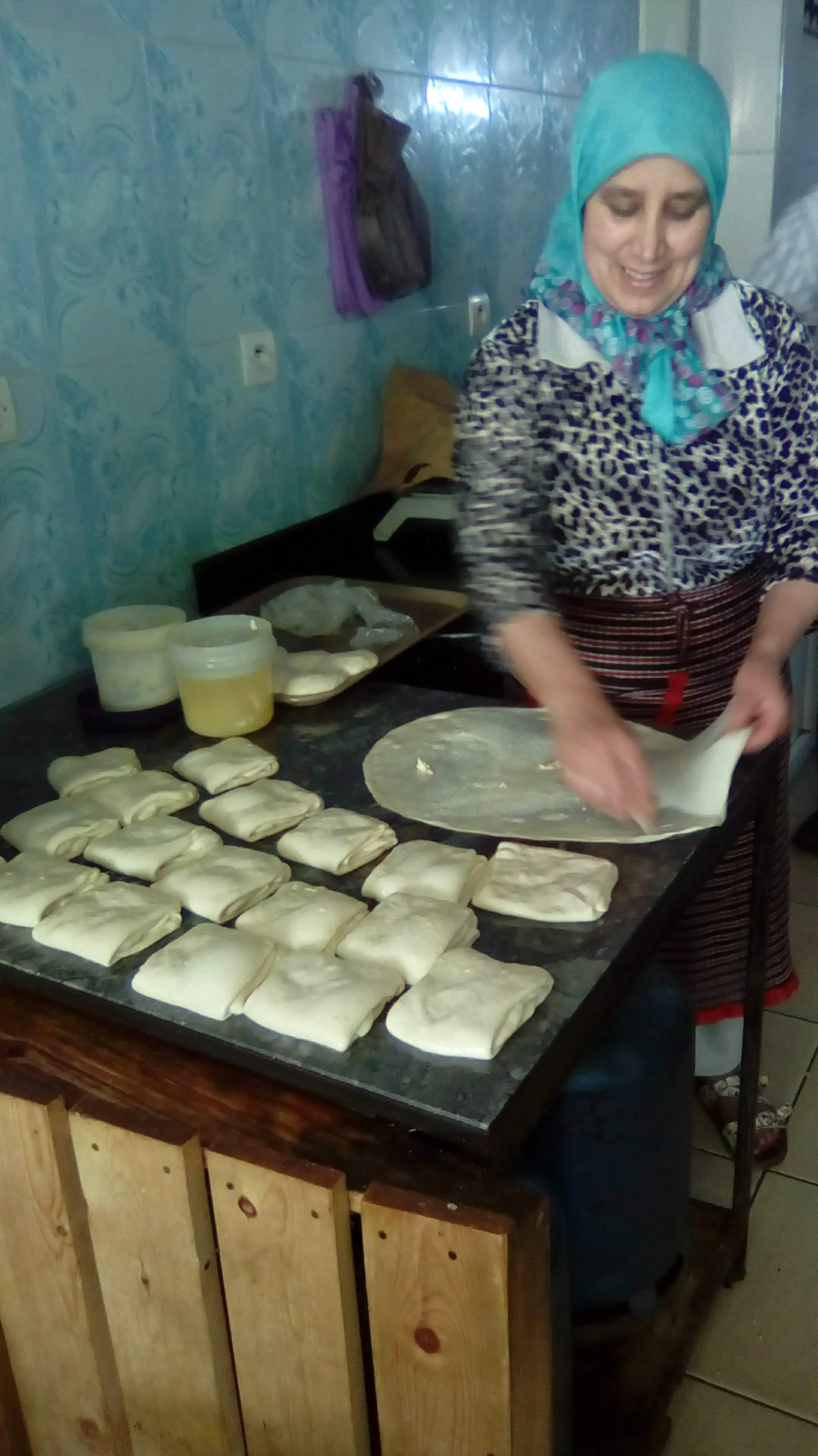 Behind the griddle out front, you can find Moroccans preparing the bread to be cooked. In this image, the woman is spreading the dough to make rghifa; the folded ones still must be stretched before going on the grill. Photo Credit: G. Szabo, Fall 2018.