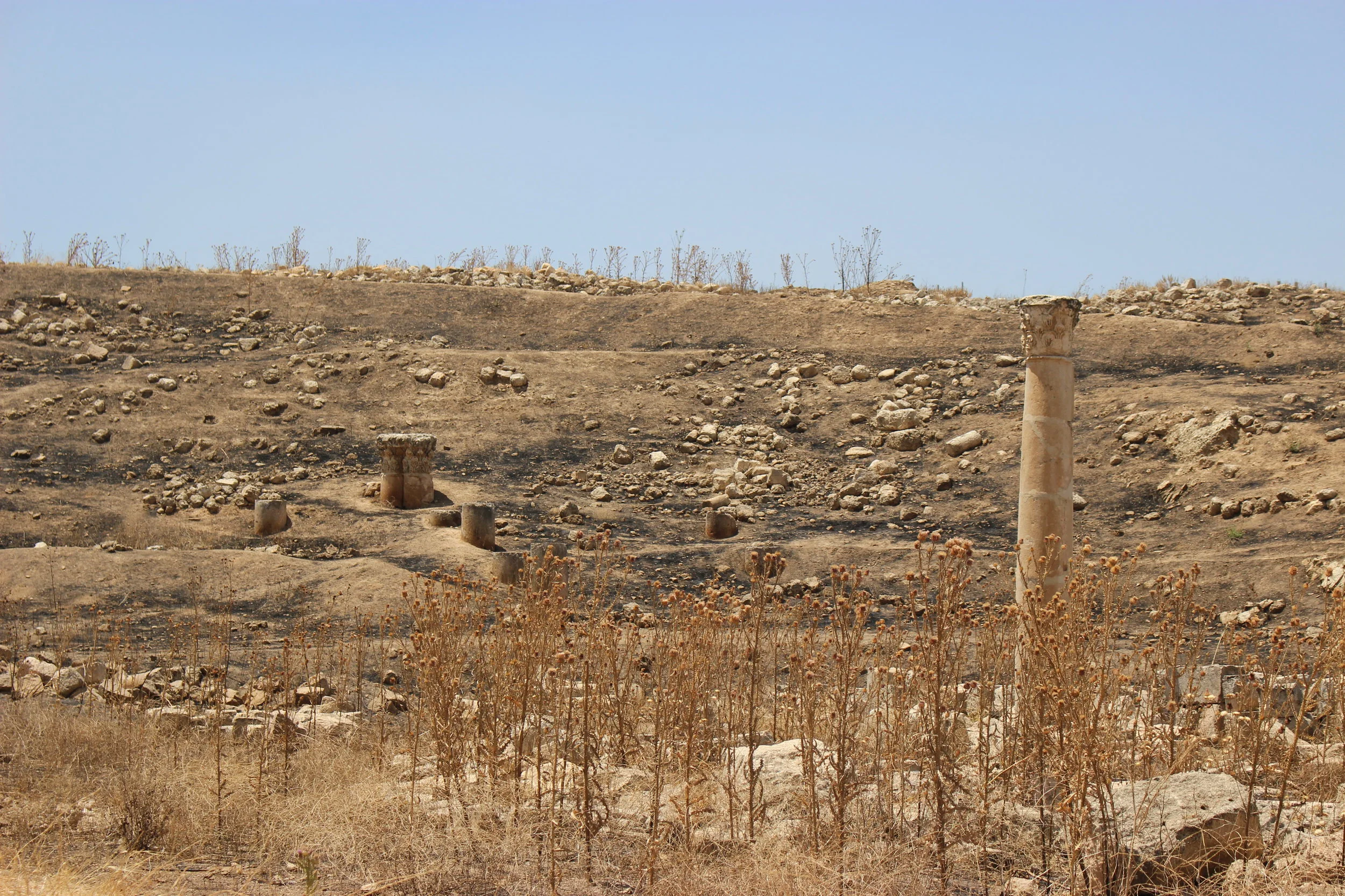 The hills above Jerash are scorched black by previous blazes. Ruins stand starkly amid the soot. Photo credit: Jessen, 2019