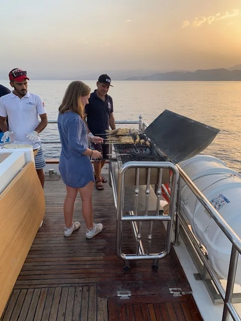 For 25 JD each, we got more than just a 2-hour boat ride at dinnertime: we also got dinner! Here, my friend Laurie was helping with the grilling. The total meal was a delicious mix of salads, meat, bread, and fish! Photo credit: Moriarty, 2019