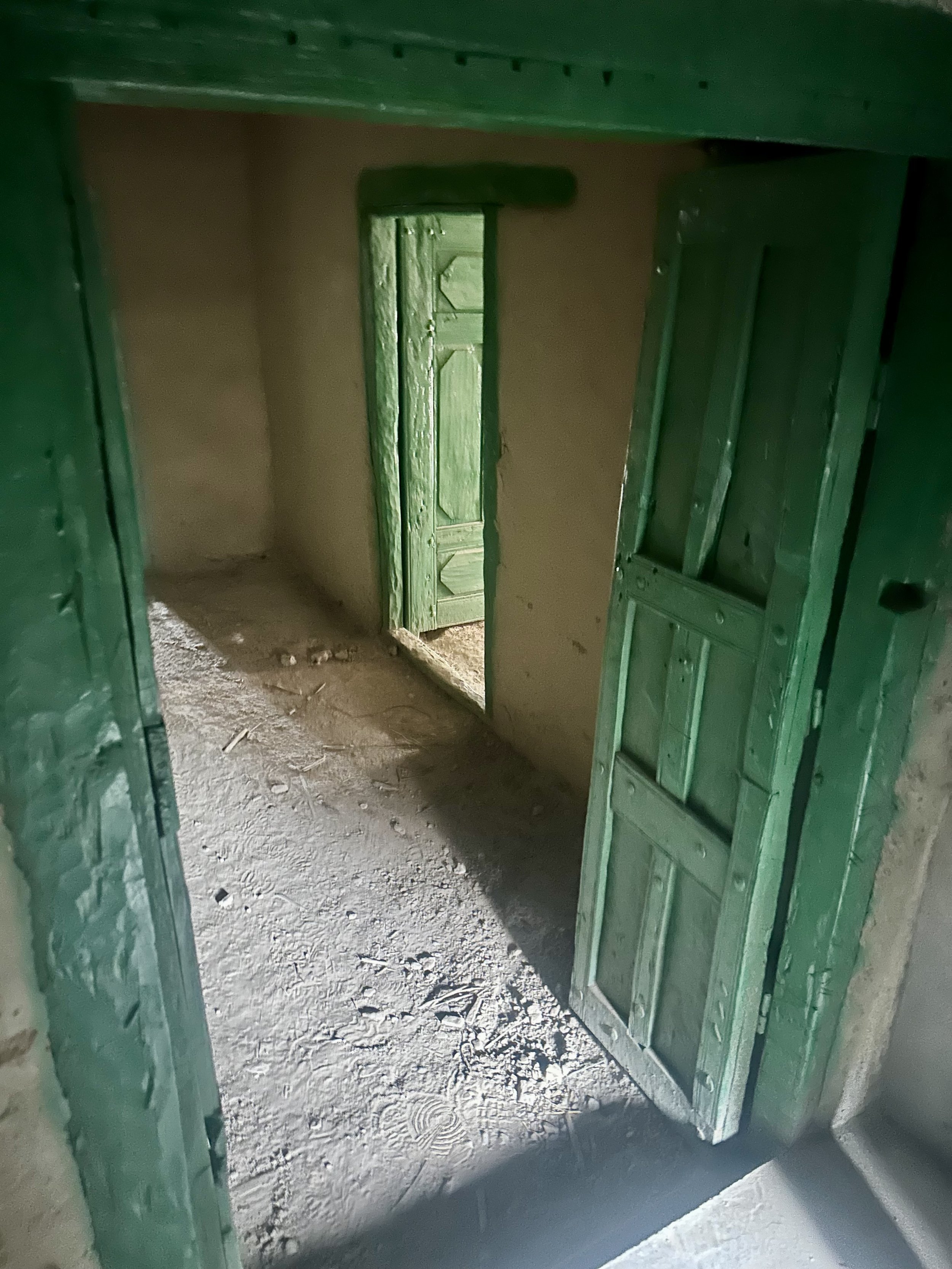 A brightly painted green doorway opens into a room with a dirt floor.