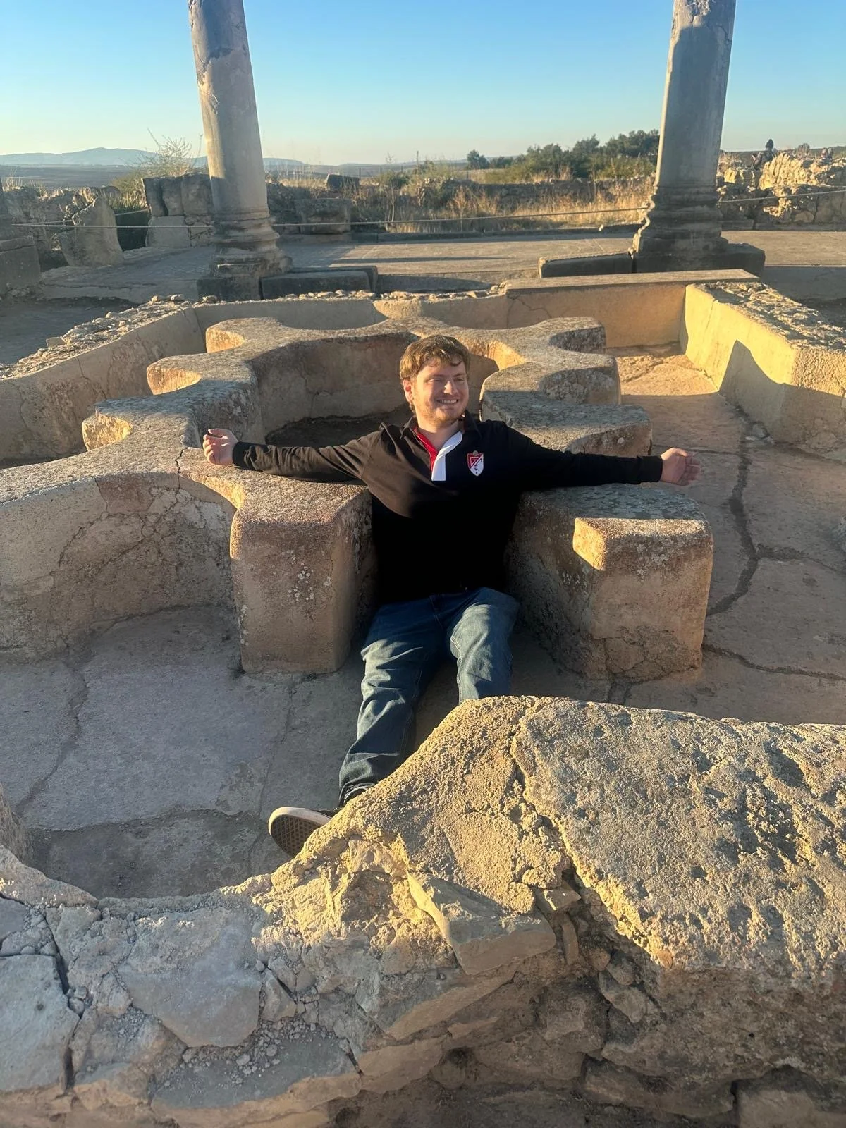 Anthony sits amongst the ruins with his arms outstretched soaking up the sun