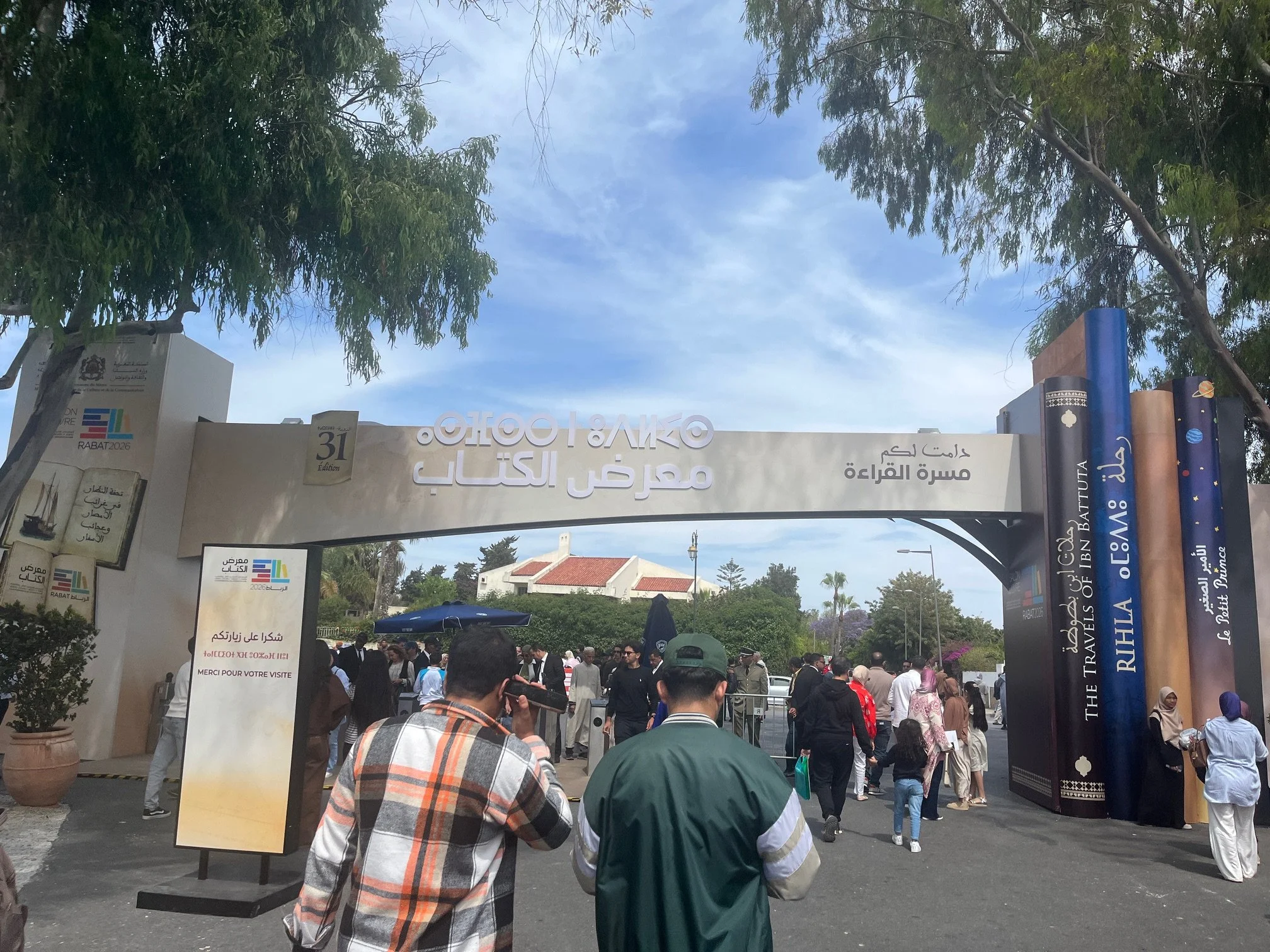 An arch welcoming people to the book fair stands outside as people walk in and out