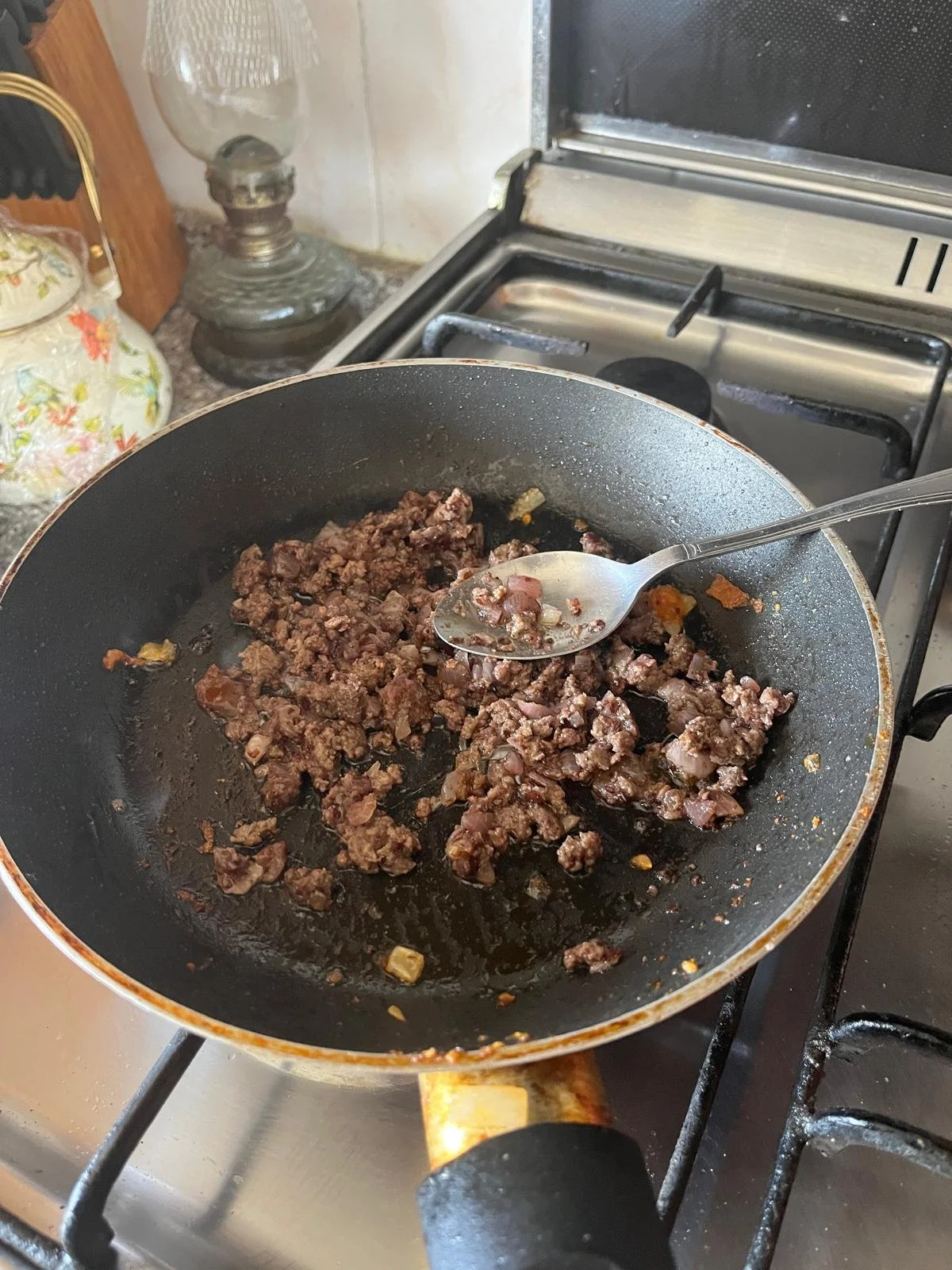 Ground beef is cooked in a skillet on the stove with a spoon to stir
