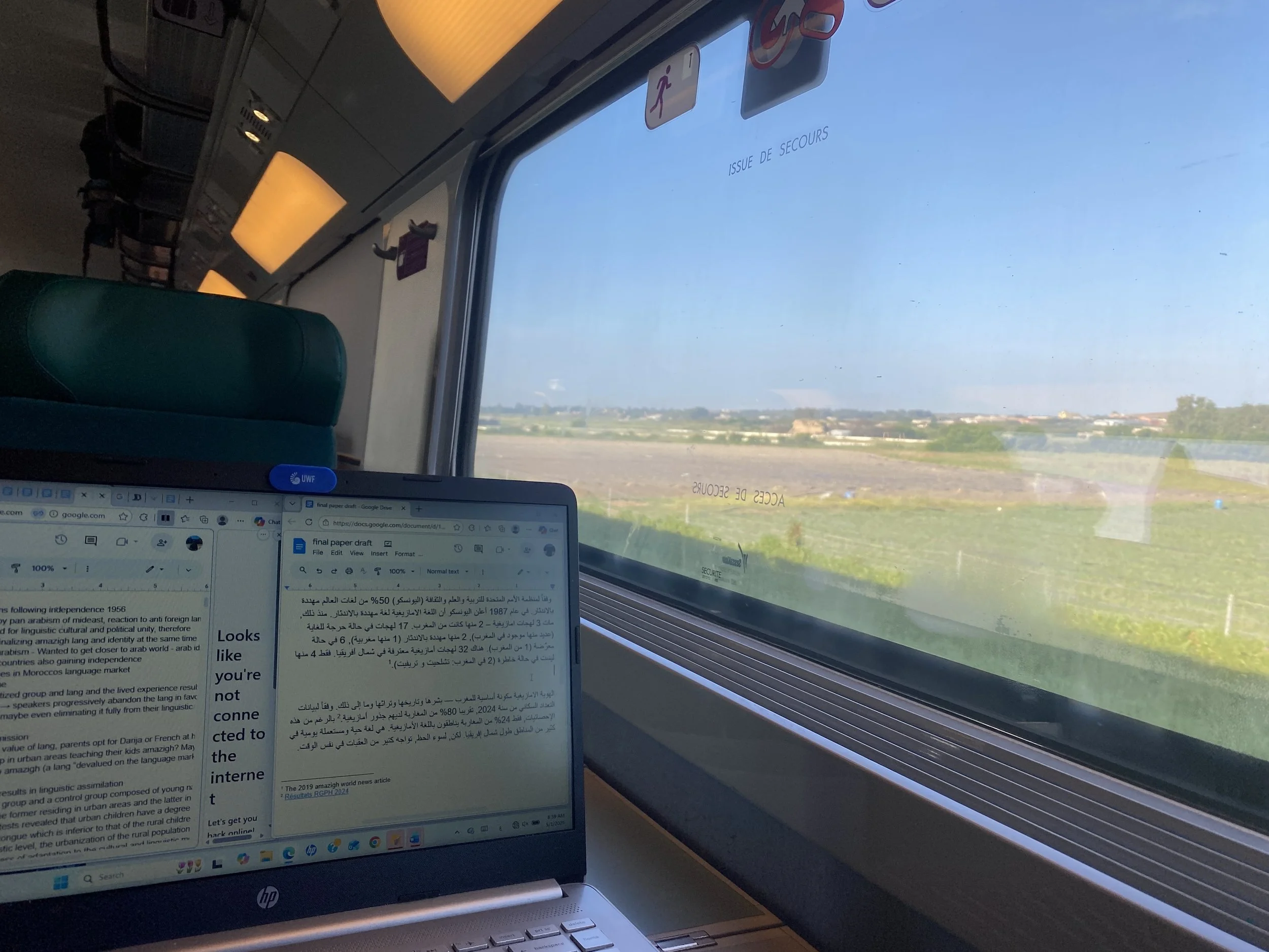 A computer sits open on a train as the countryside goes by