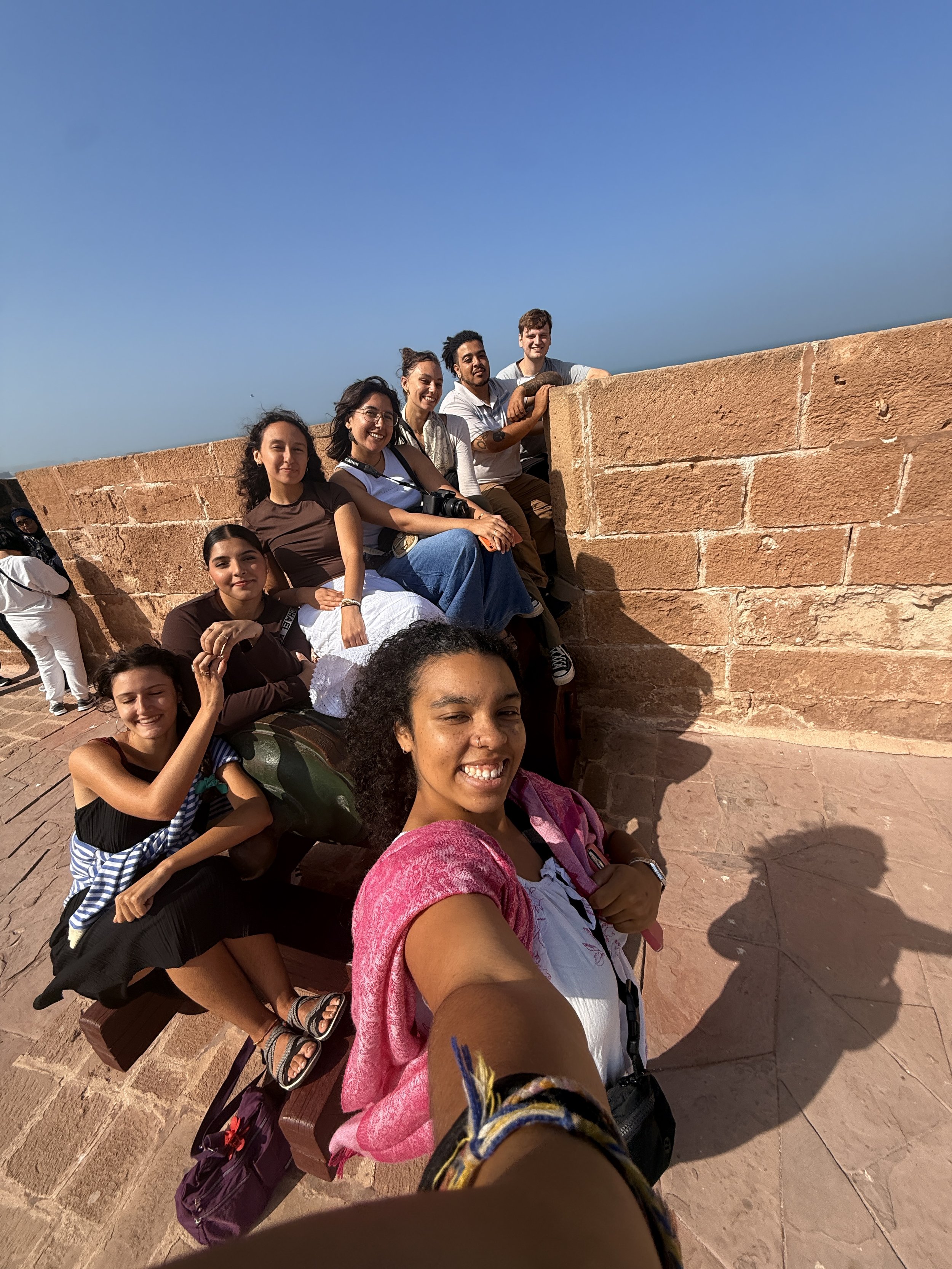 A group of young people take a selfie sitting on and in front of a stone wall