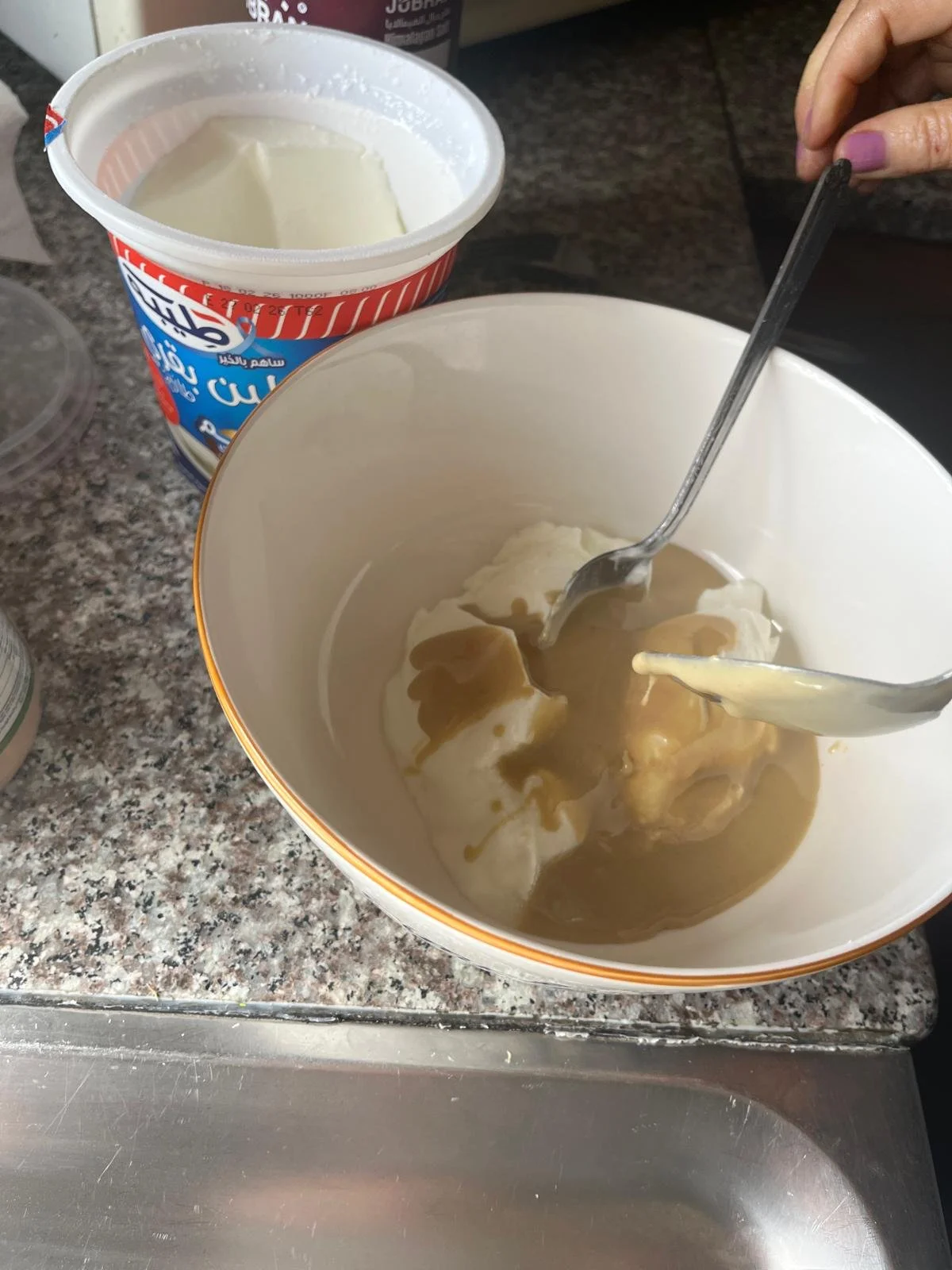 With two spoons, someone stirs in tahini into leben in a bowl