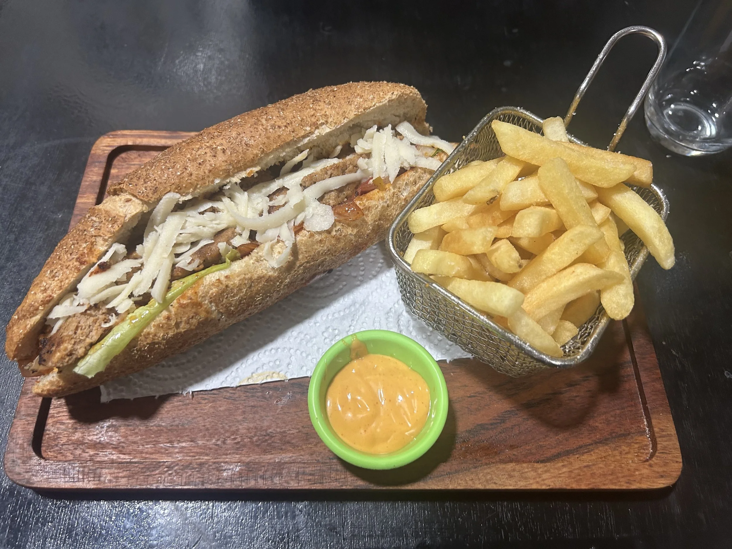 A chicken sandwich sits on a wooden tray with a hopper of fries