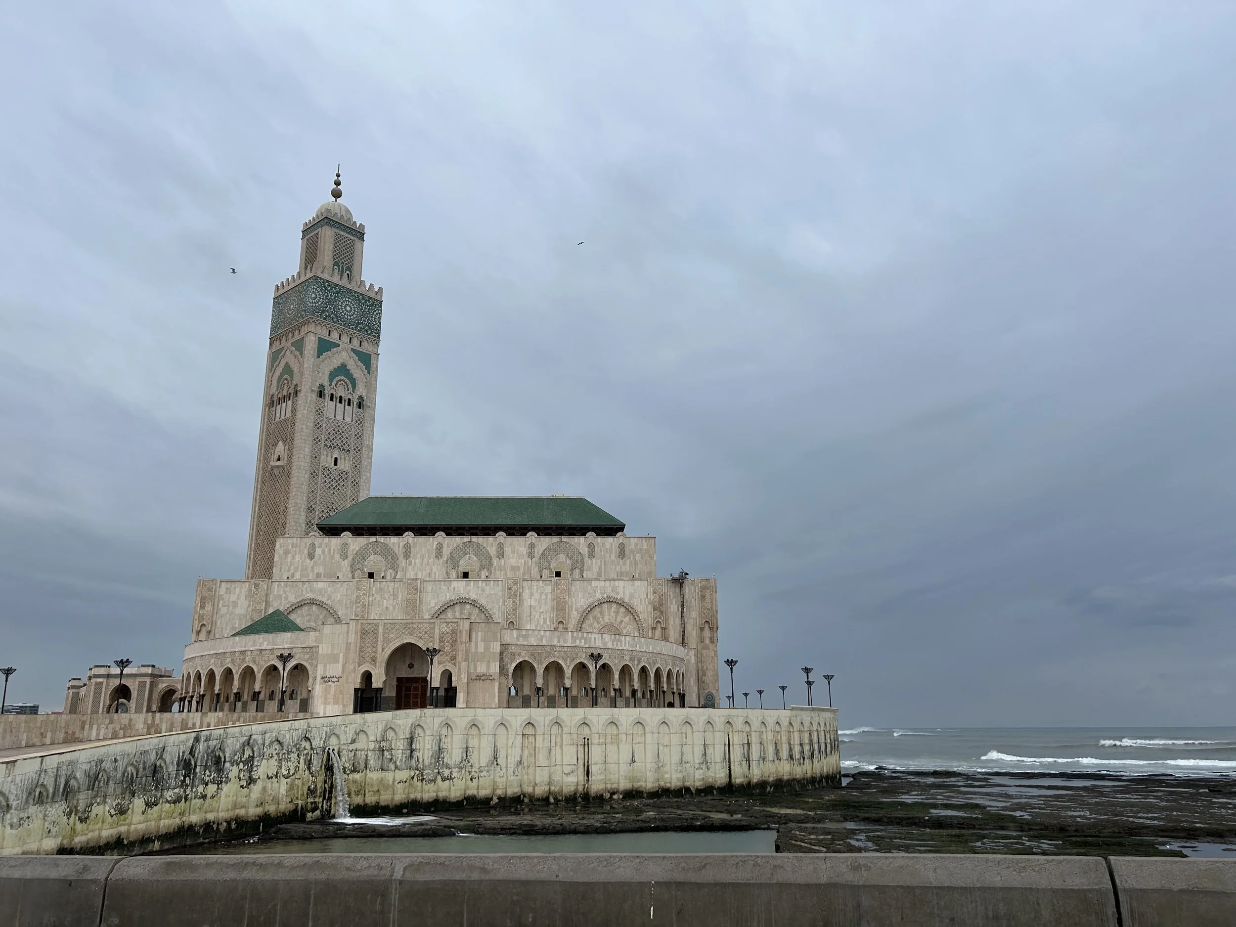 The mosque in Casablanca rises above the sea on a cloudy day. Its minaret reaches far in the sky
