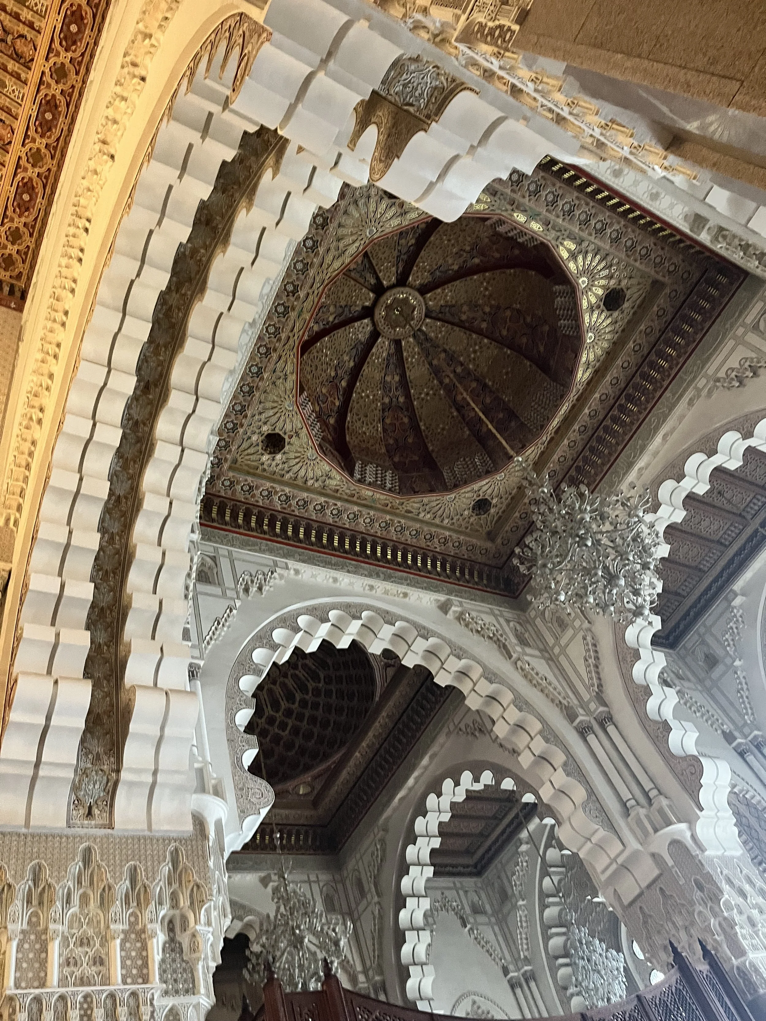Looking up at the ornate carved ceiling of a mosque, specifically into a muqarnas dome