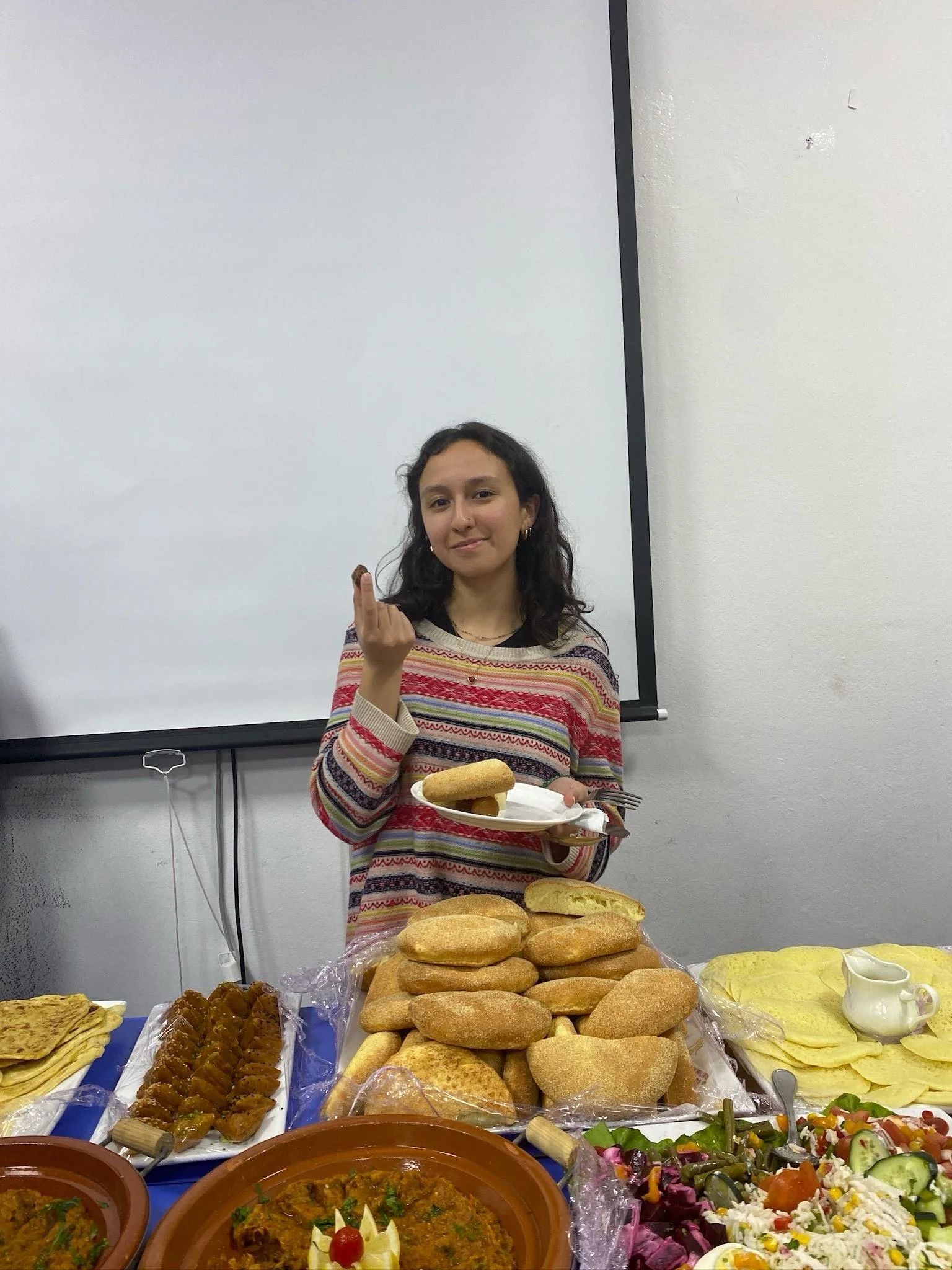 A student sits and eats from a plate behind a table covered in platters of food.
