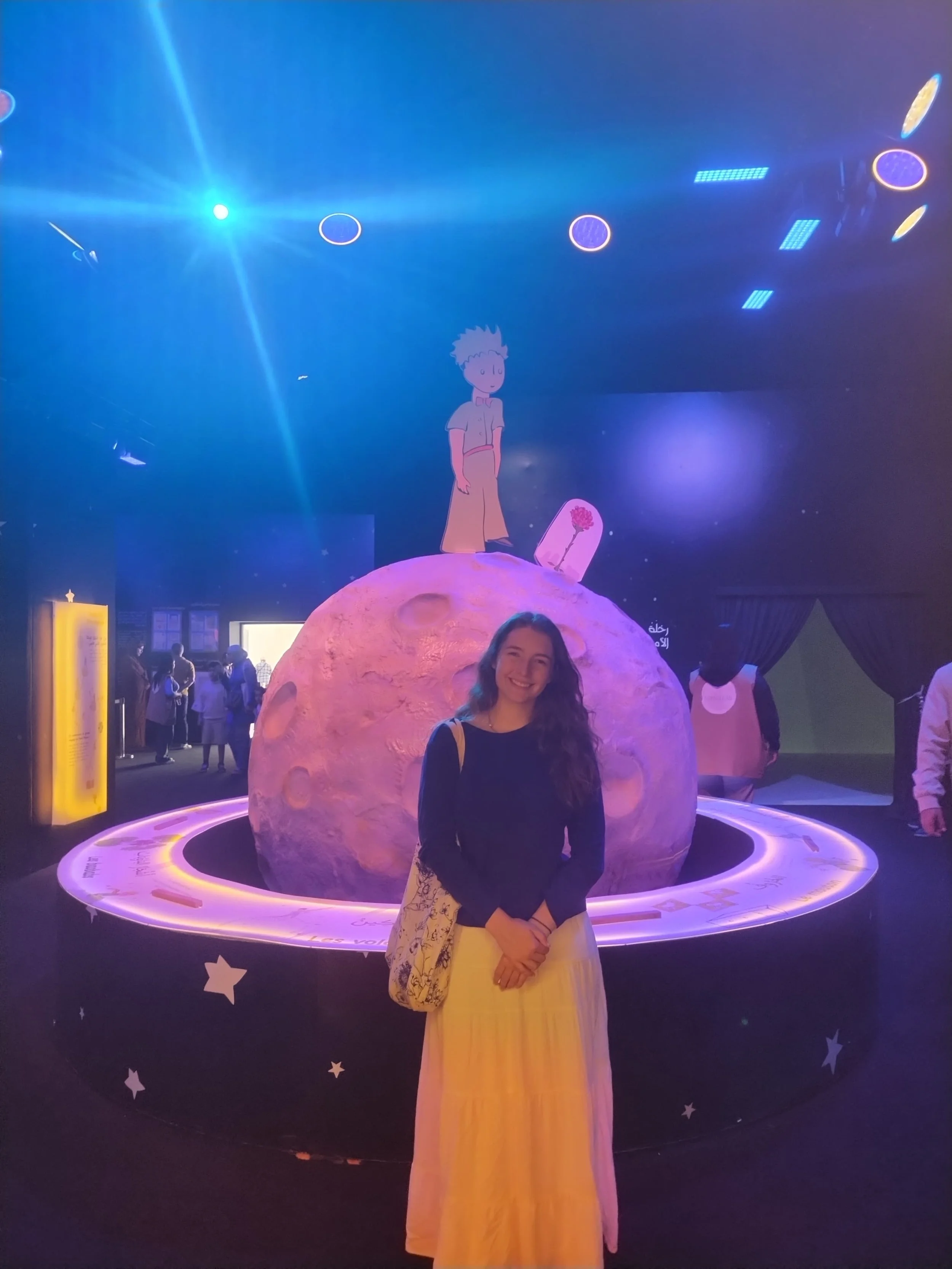 Claire stands in front of a model of Saturn with the Little Prince on top