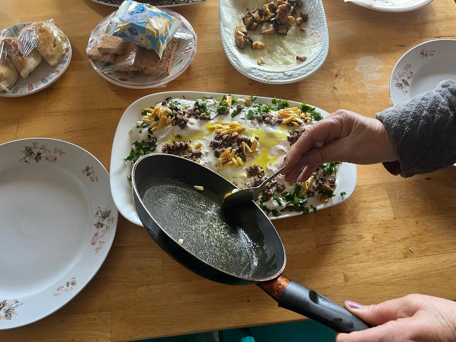 Someone scoops toasted nuts and olive oil on top of a dish of food.