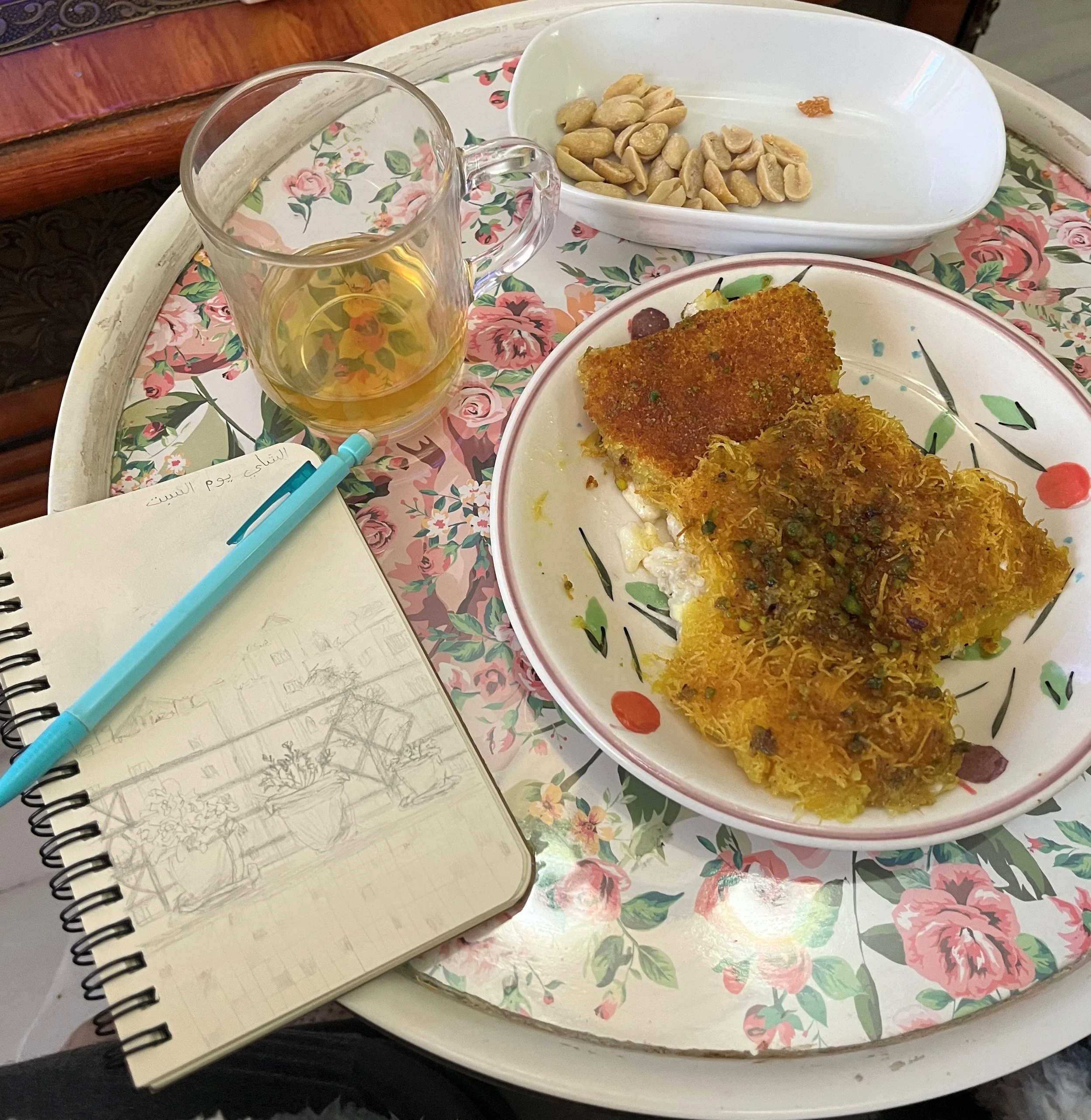 A small table holds a notebook and pen, a plate with a sweet treat and a cup of tea