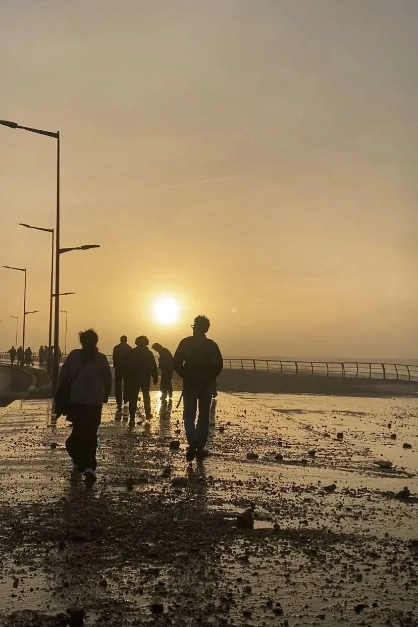 People walk on a boardwalk into the sunset and water seems to come up from the side spilling onto the path
