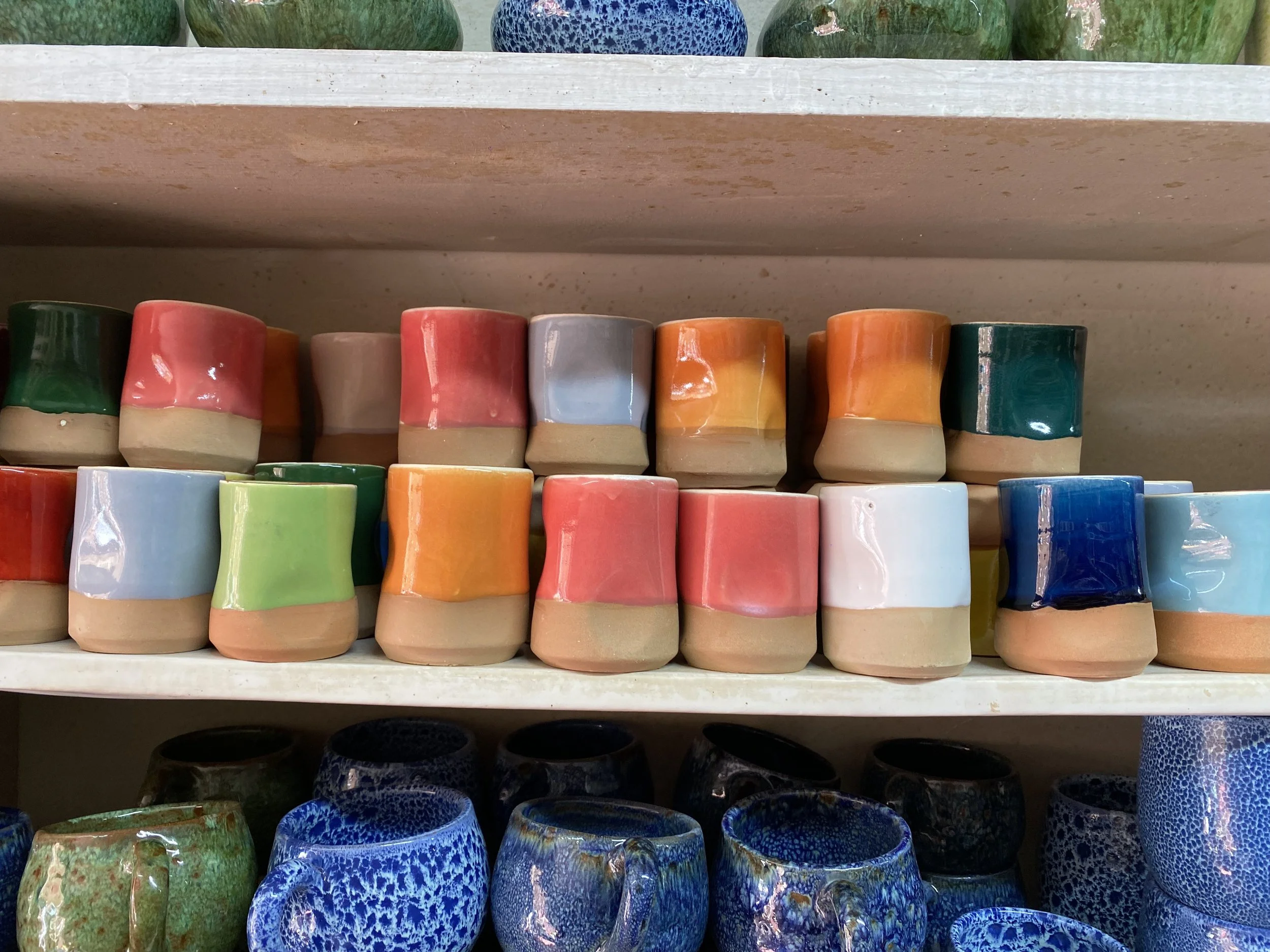 Shelves full of simple glazed clay cups in different colors.