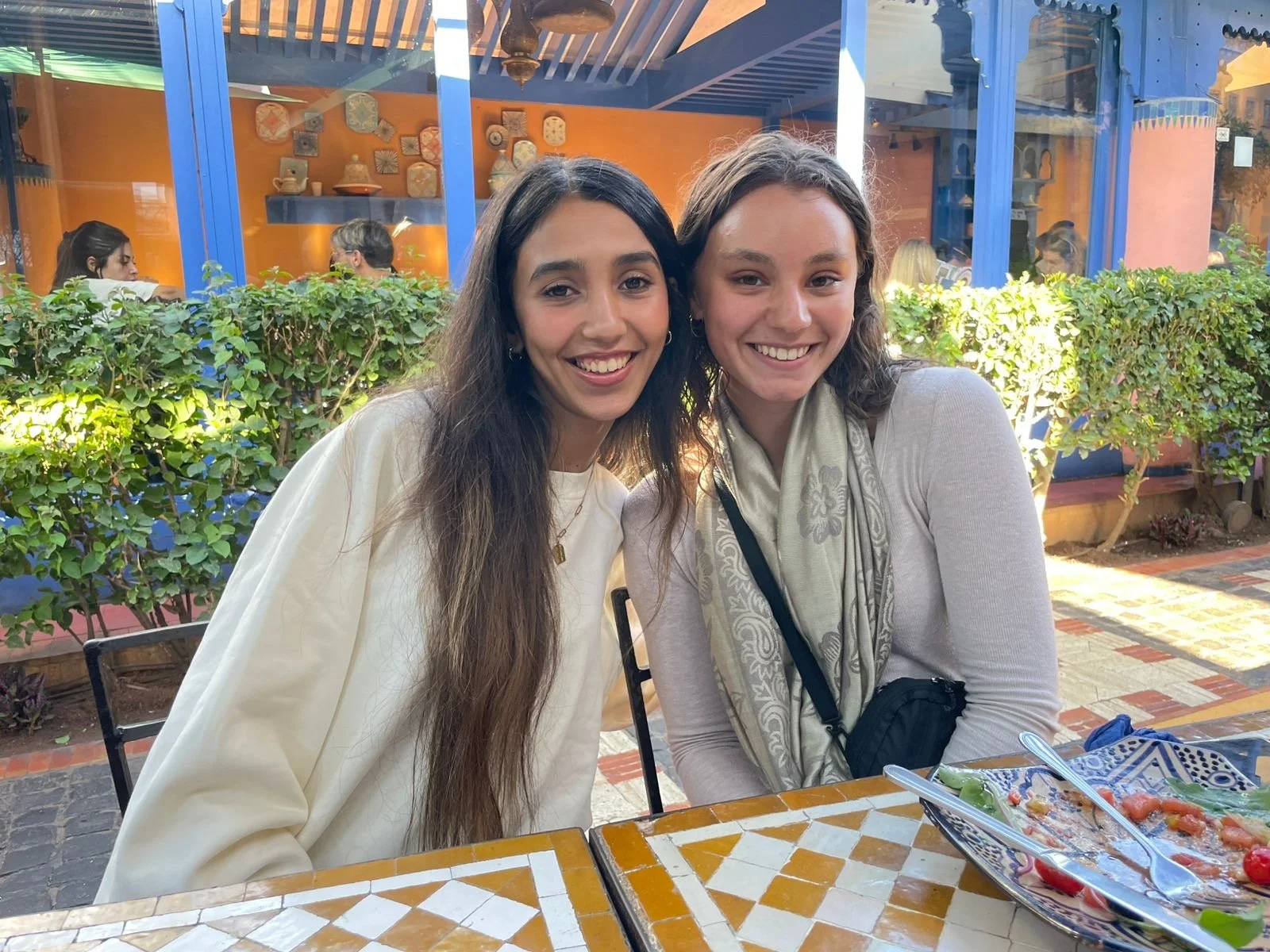 Two young women sit at a restaurant table and smile for the camera.