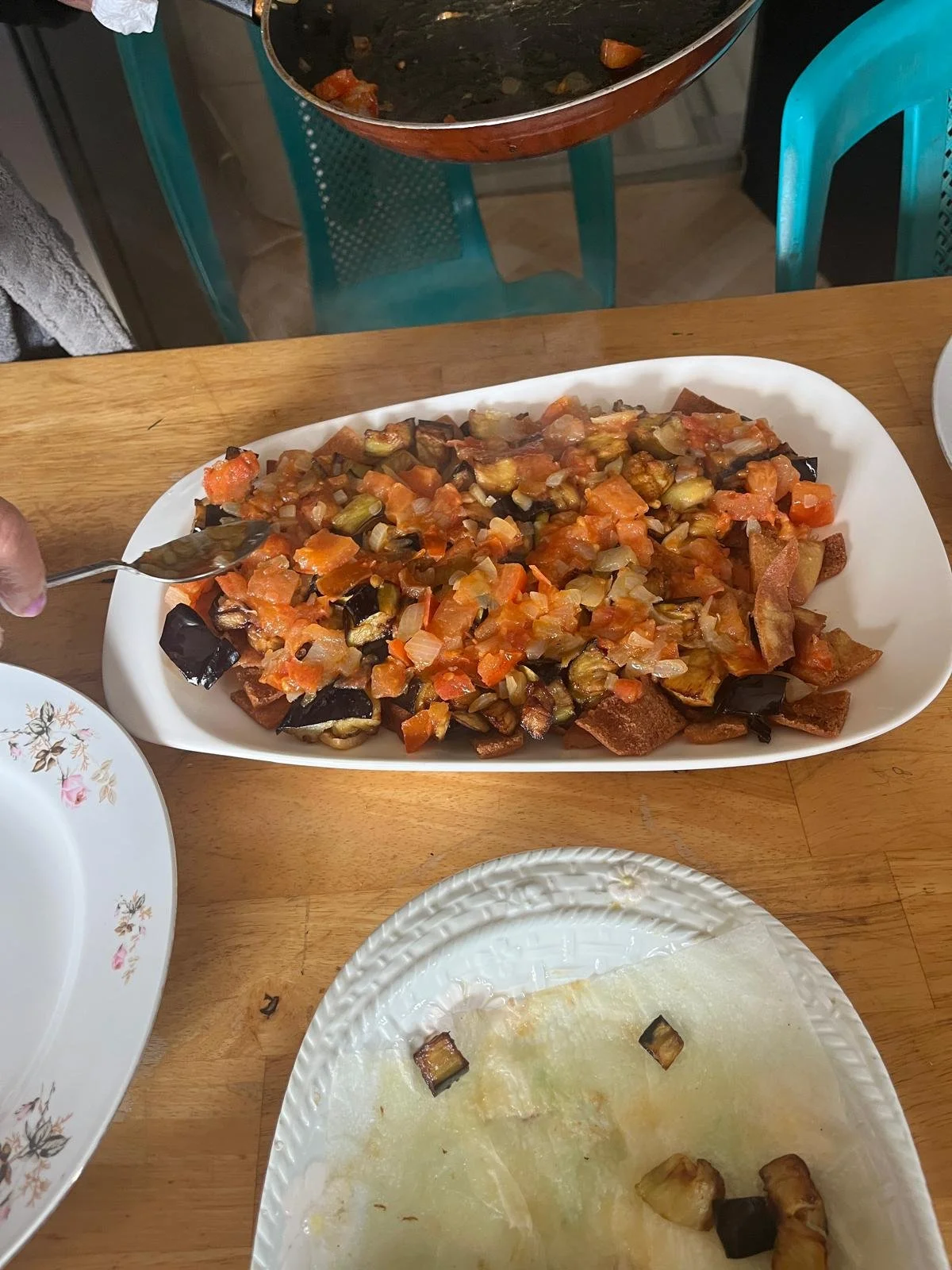 Tomato is added on top of a layer of eggplant and fried flatbread on a dish