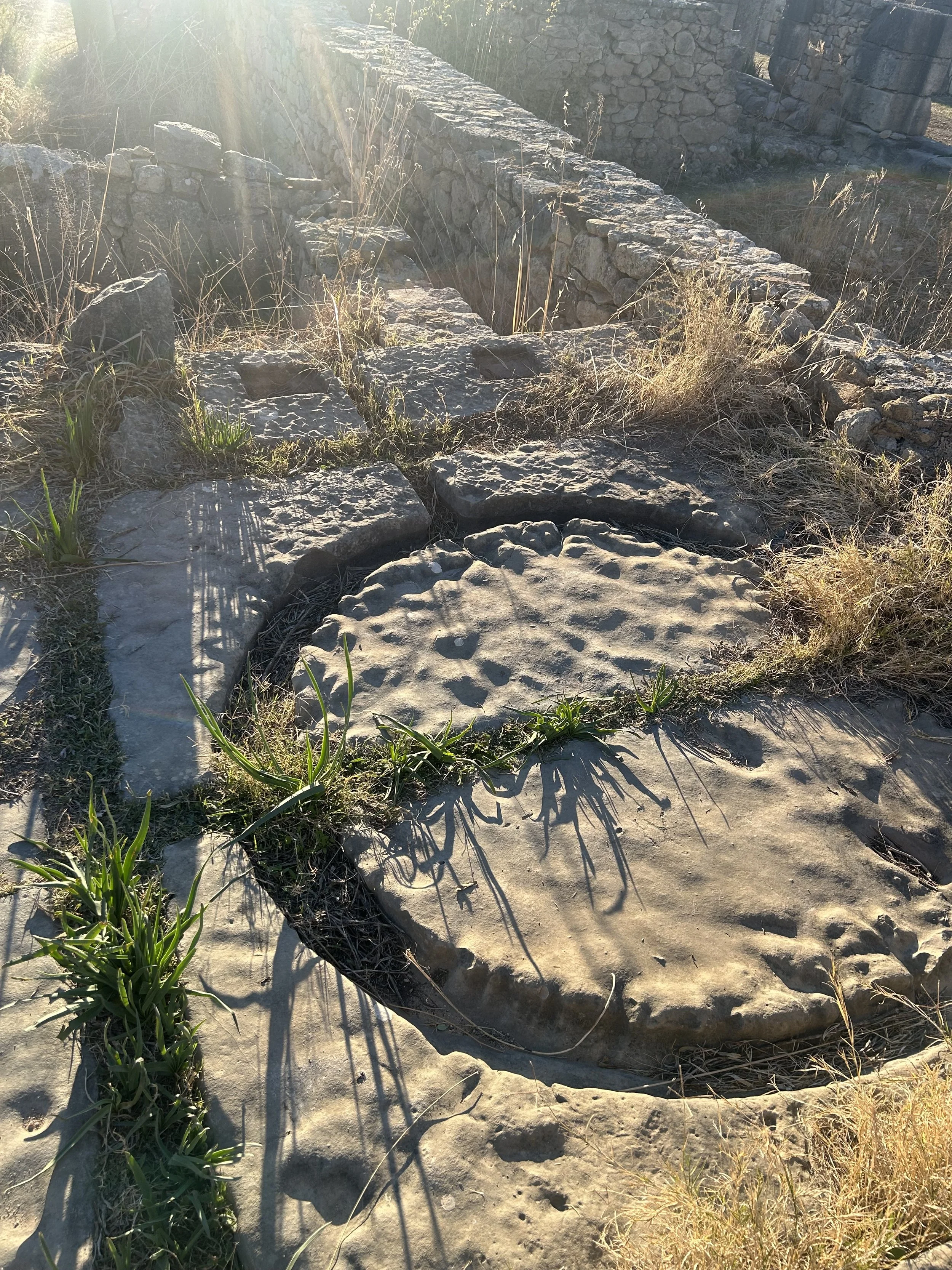 Ancient ruins of an oil press have grass growing up between the cracks