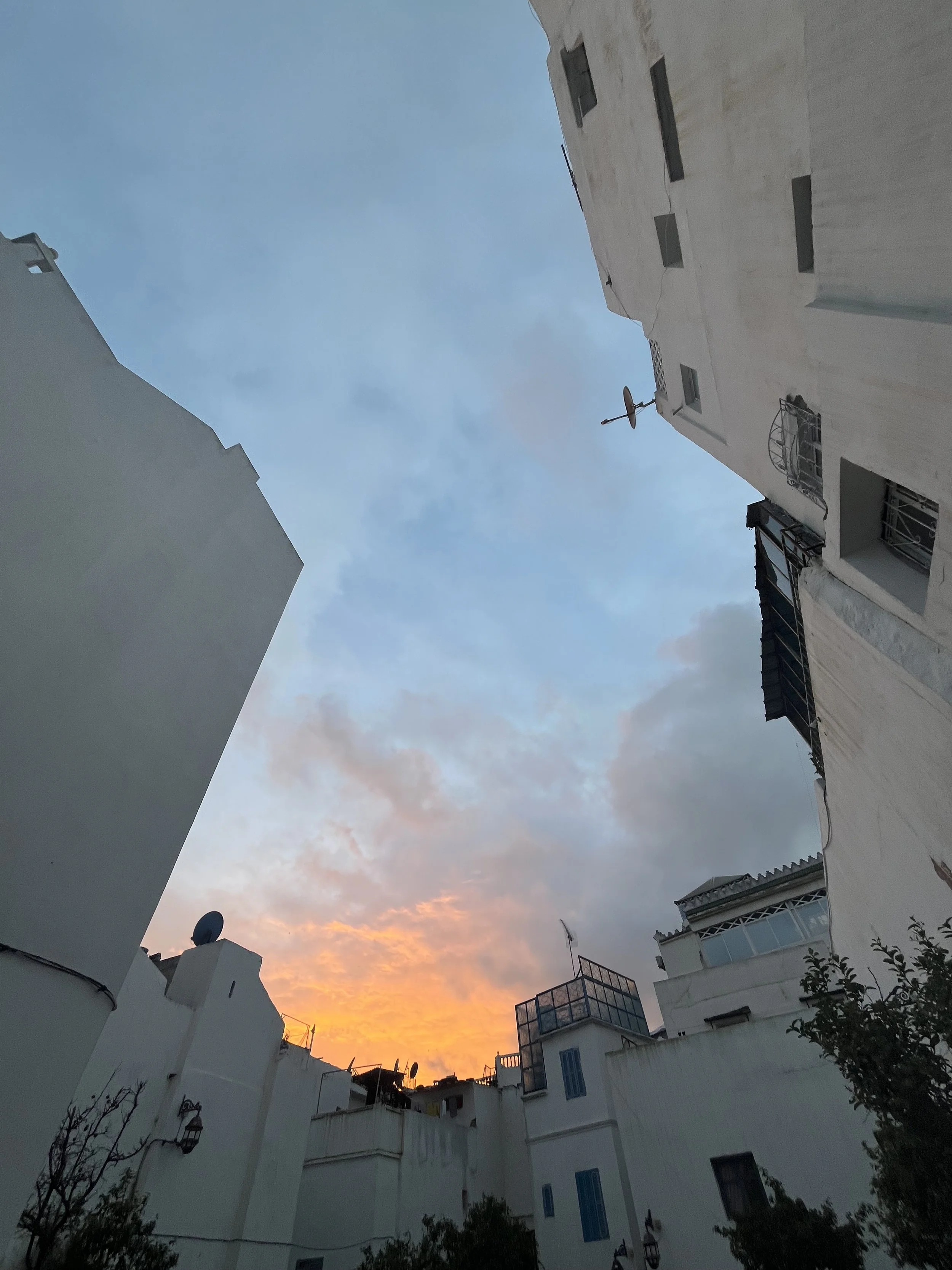 Looking up from among white residential buildings into the clouds which are orange and pink from sunset