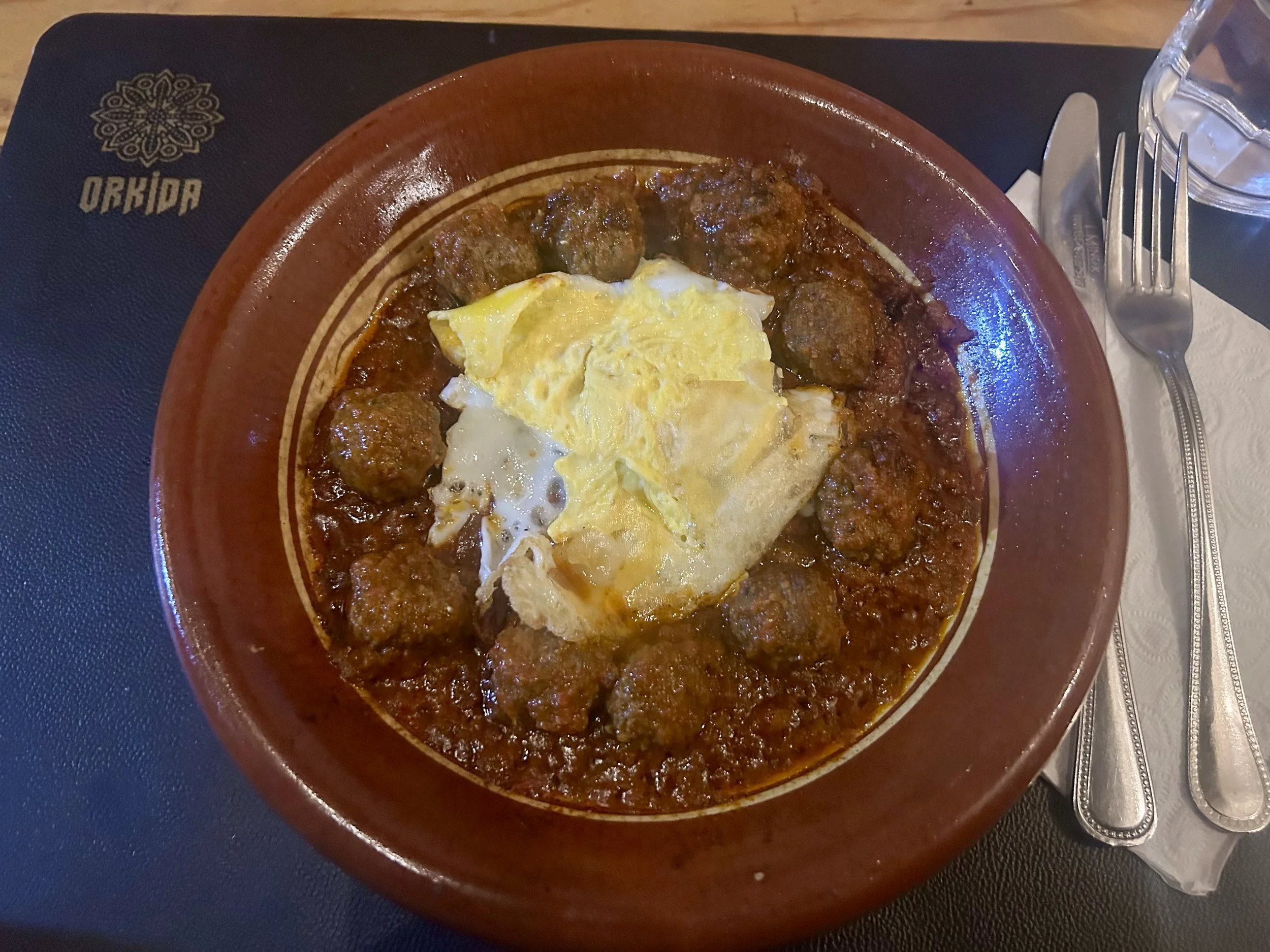 A tagine like bowl holds meatballs in a tomato based sauce with an egg on top