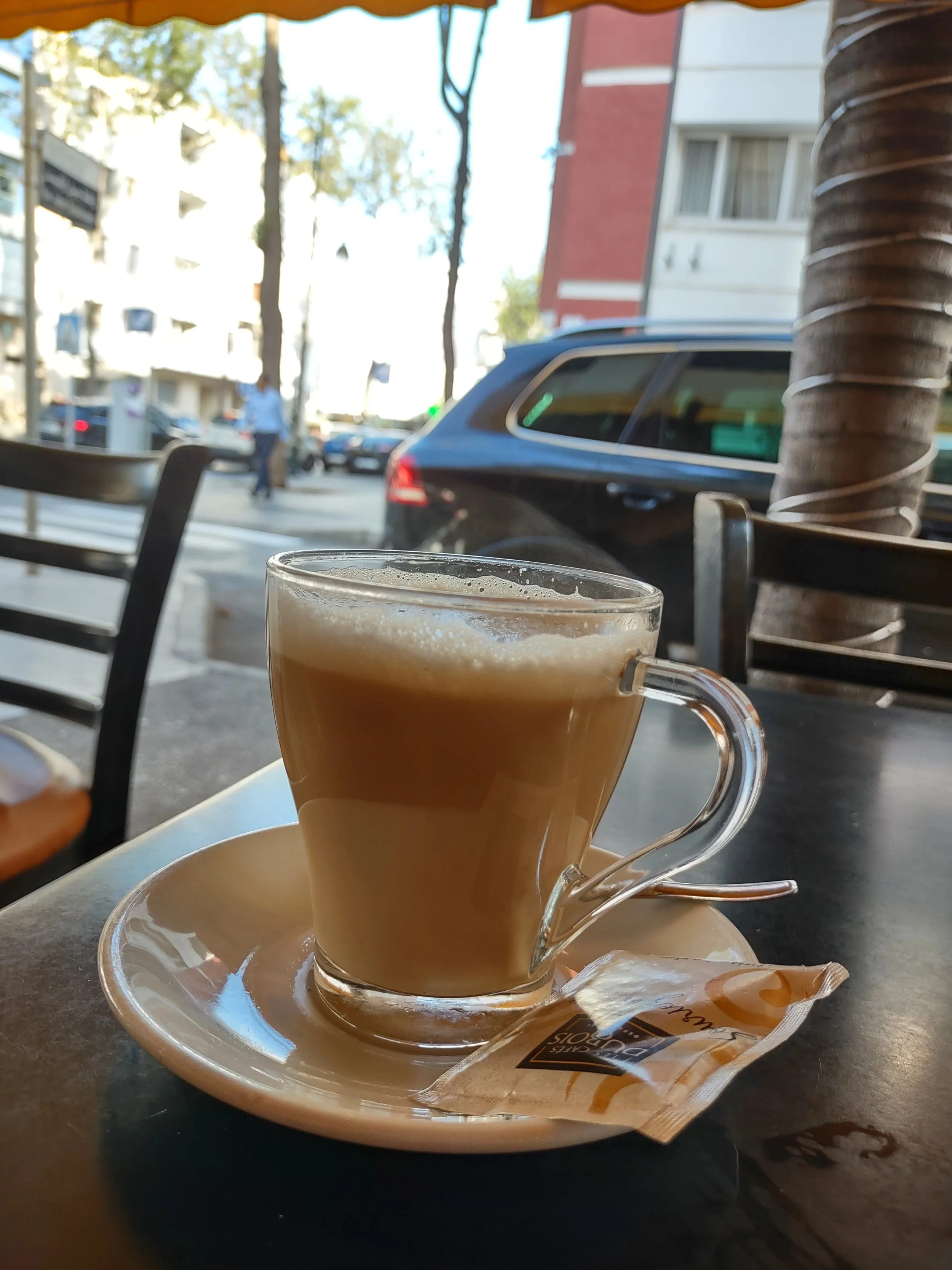 A coffee in a glass mug on a saucer with sugar packet