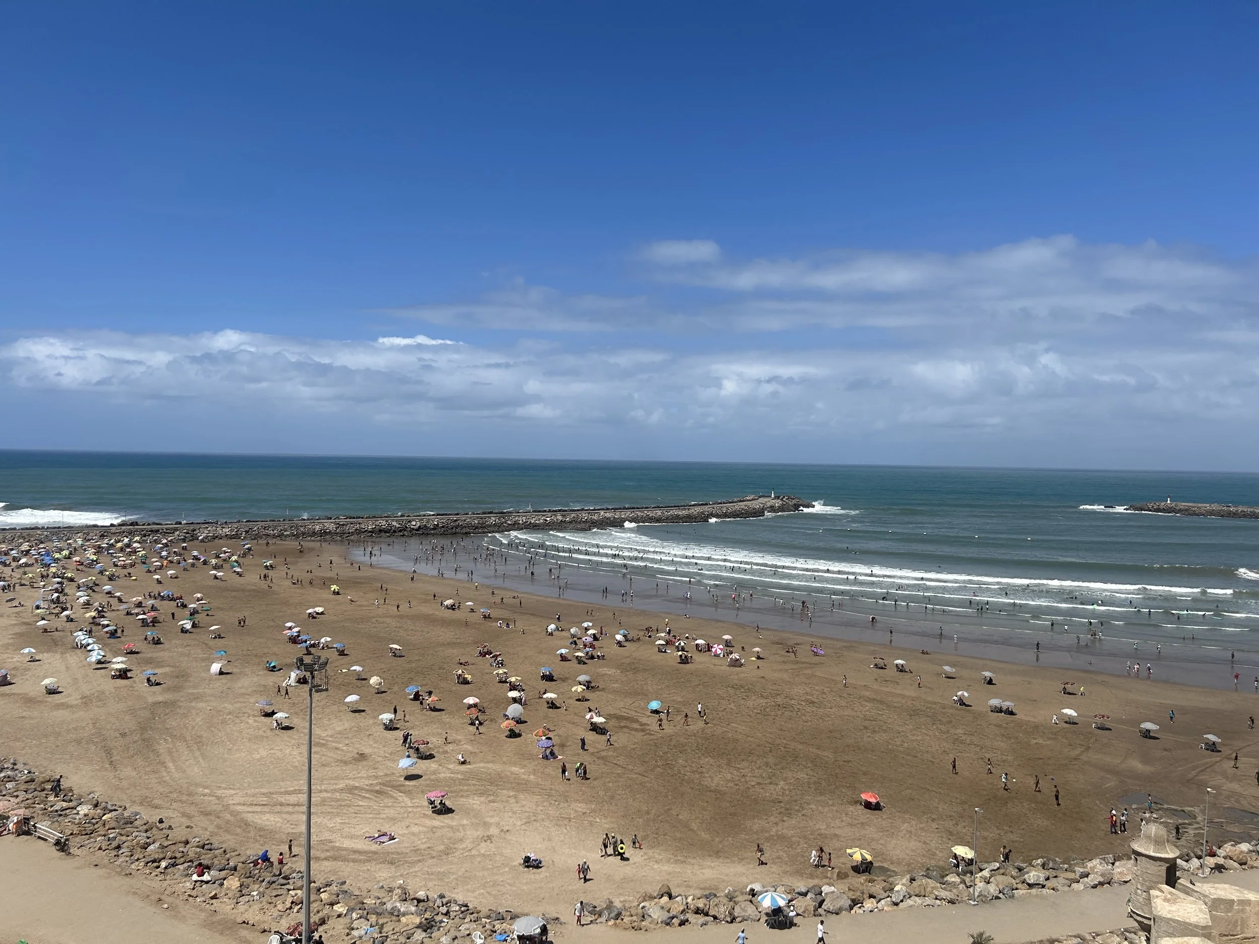 The Rabat beach is wide and protected by a rock wall that stretches into the ocean. People have umbrellas on the beach