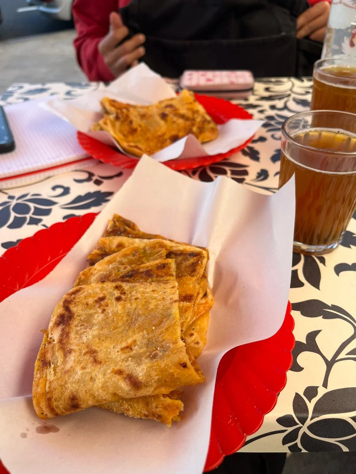 Two plates of thin Moroccan bread folded up sit on a table with a white and black design next to two cups of Moroccan tea